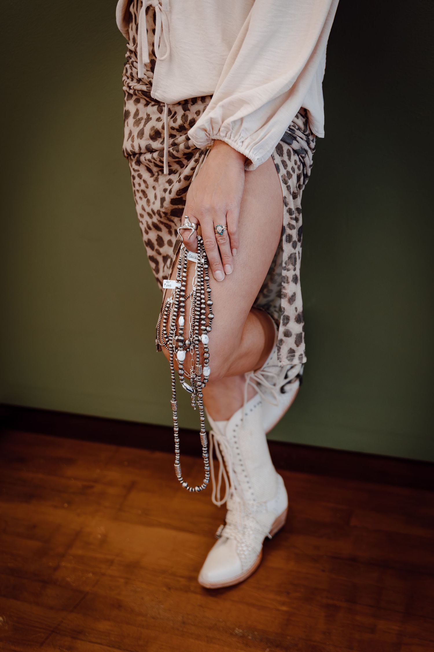 A North Platte, Nebraska lifestyle brand session woman holds dangling beaded necklaces against a green wall.