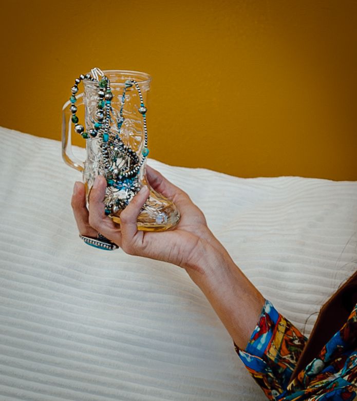 A North Platte, Nebraska lifestyle session hand holds up a glass mug decorated with sparkling turquoise jewelry and beads.