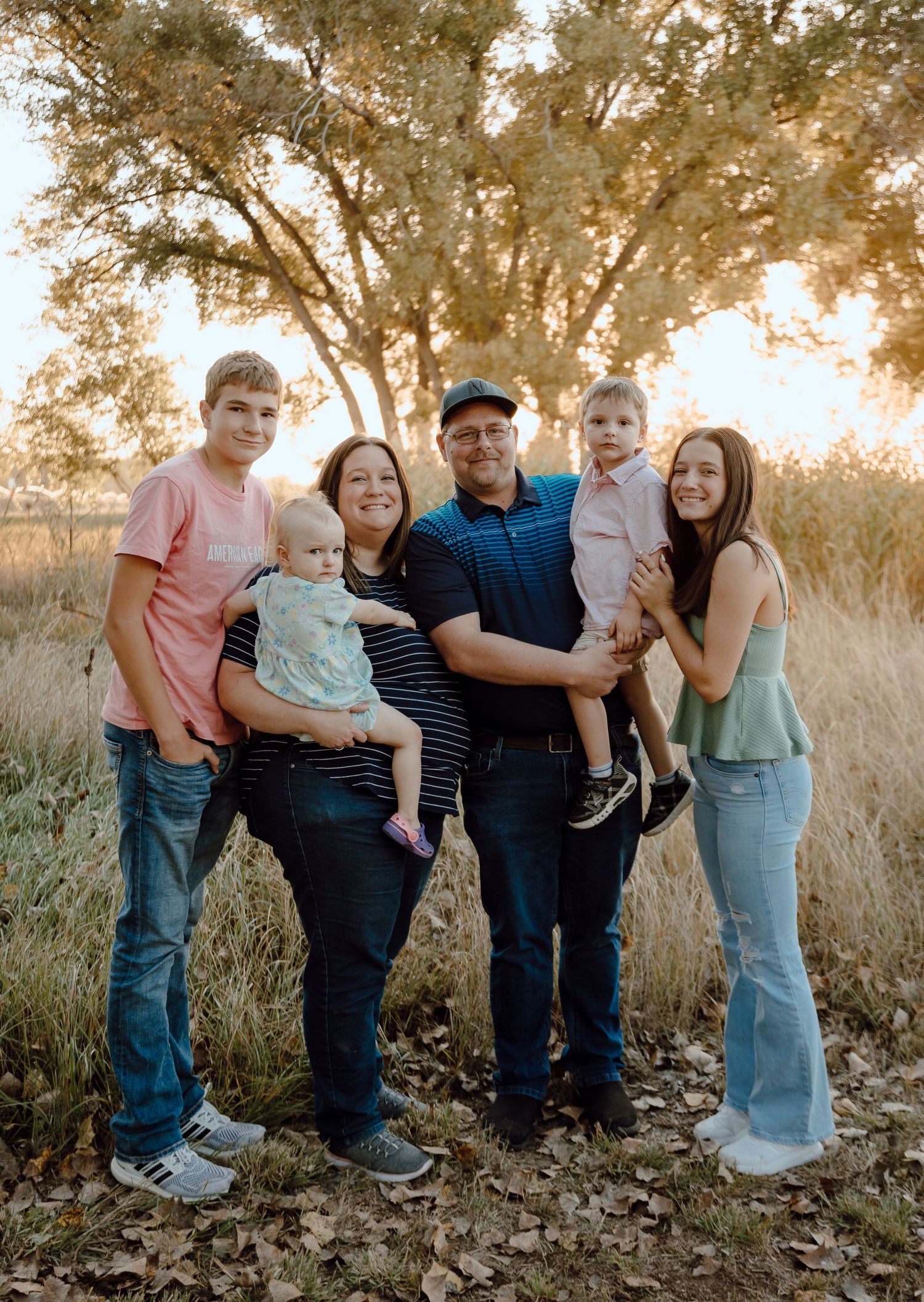 A Paxton, Nebraska lifestyle family session family stands together during a sunset photoshoot in a golden field of tall grass.