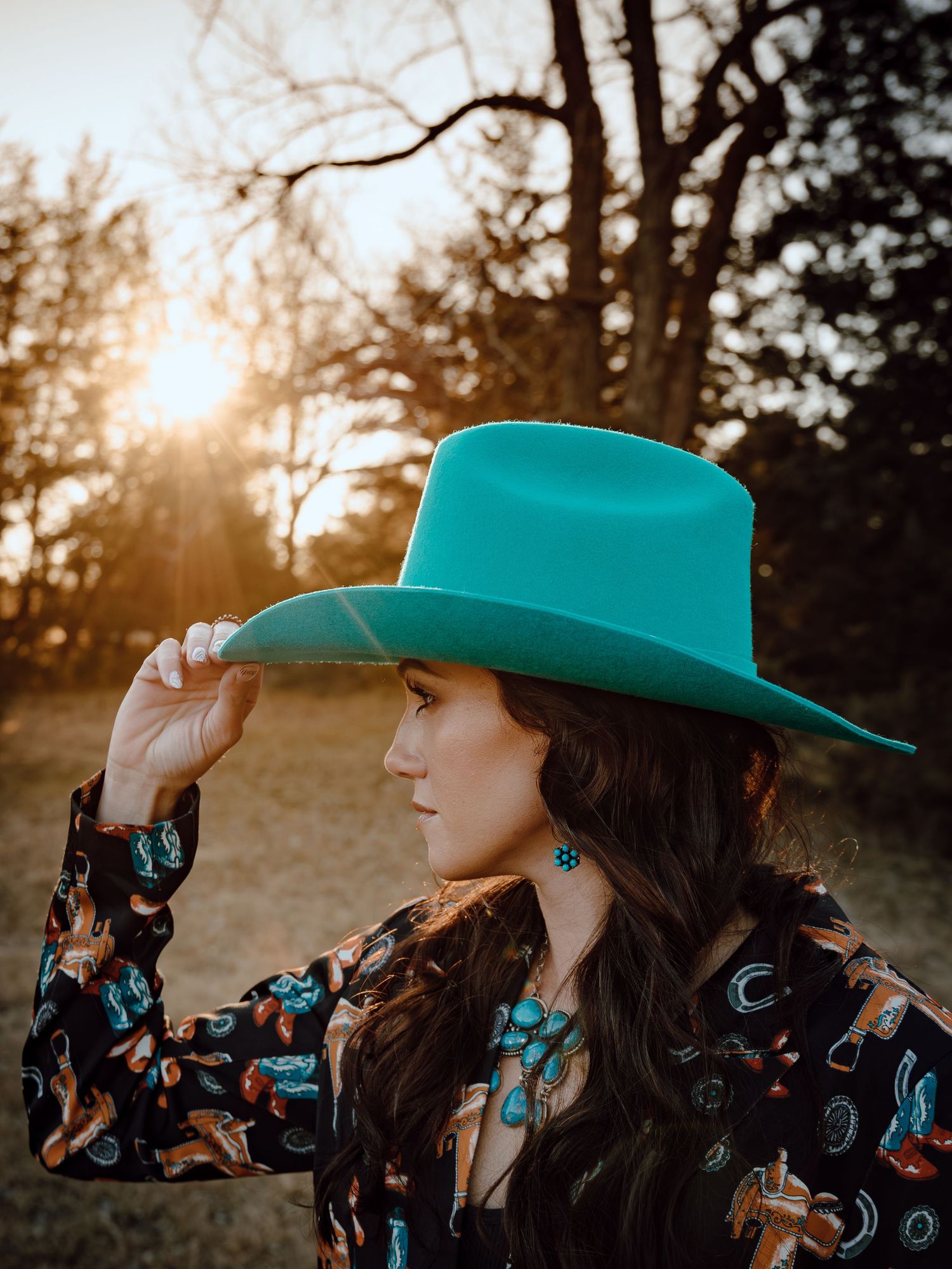 A North Platte, Nebraska lifestyle brand session woman in a turquoise cowboy hat poses in golden sunlight.
