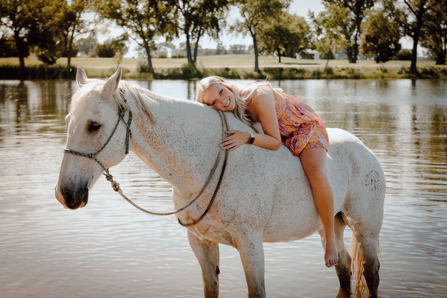 A Chappell, Nebraska lifestyle senior session girl in a pink dress poses gracefully with a gray horse in lake water.