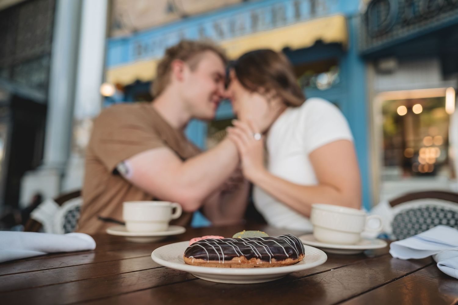 Couple sharing a romantic moment at a Utah cafe table with a chocolate eclair in the foreground.