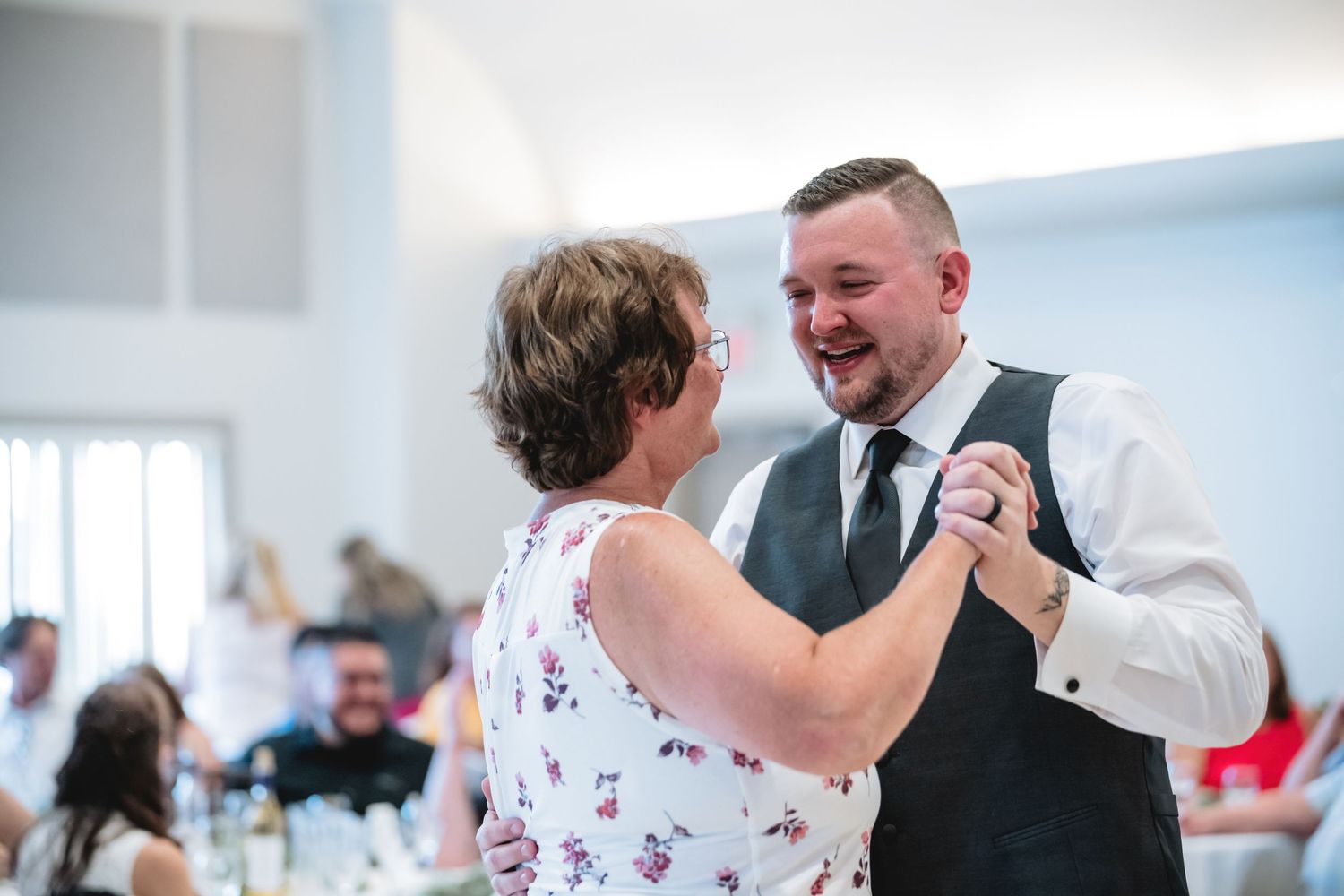Groom dancing joyfully with a woman in a floral dress at a wedding reception.