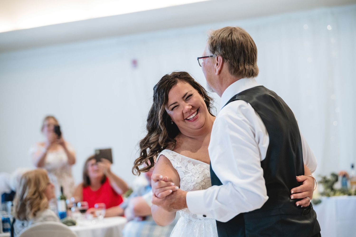 Bride laughing joyfully during first dance with groom at elegant wedding reception.