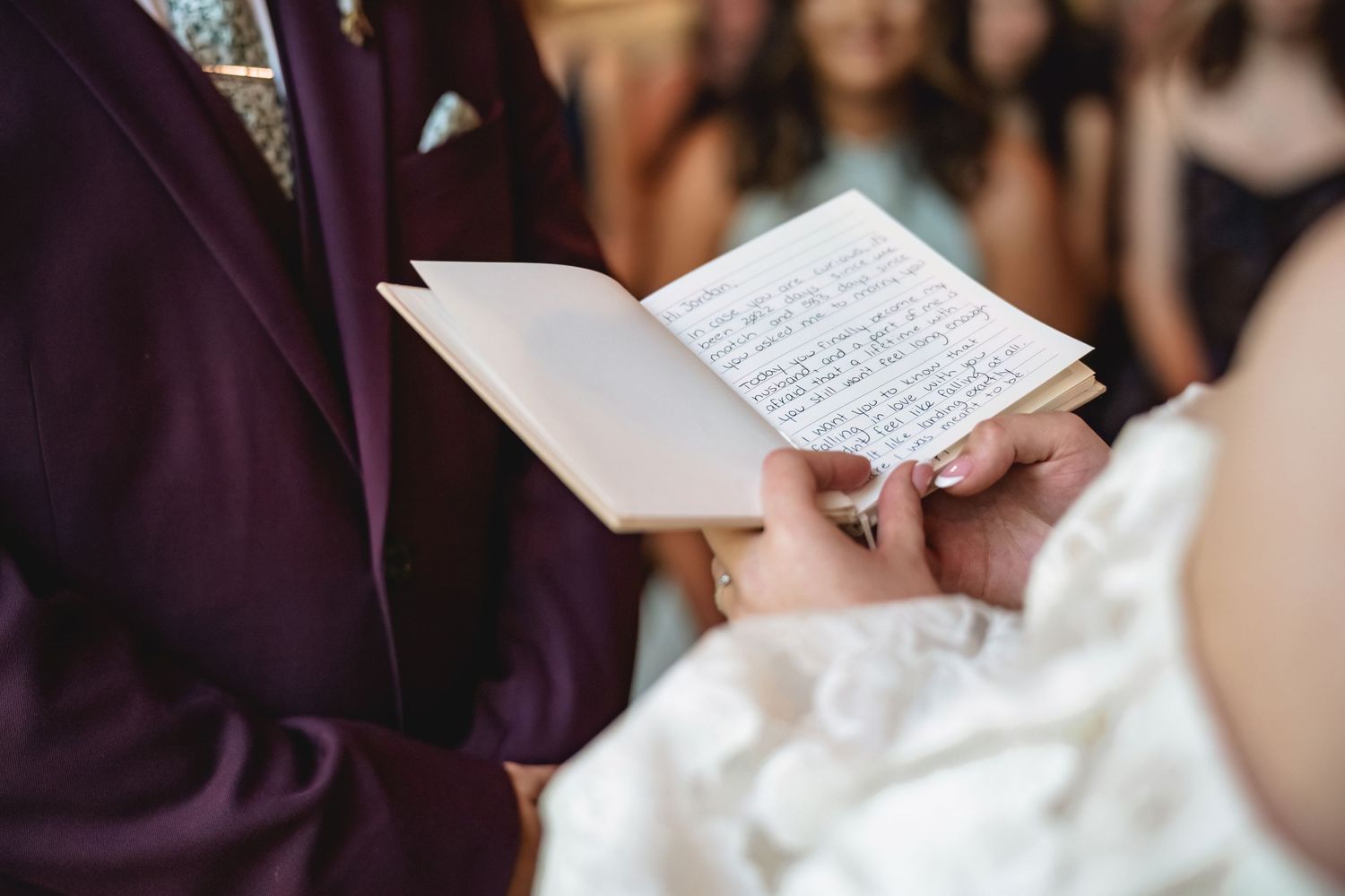 Bride reading handwritten wedding vows from a small booklet during a ceremony, wearing a white dress.