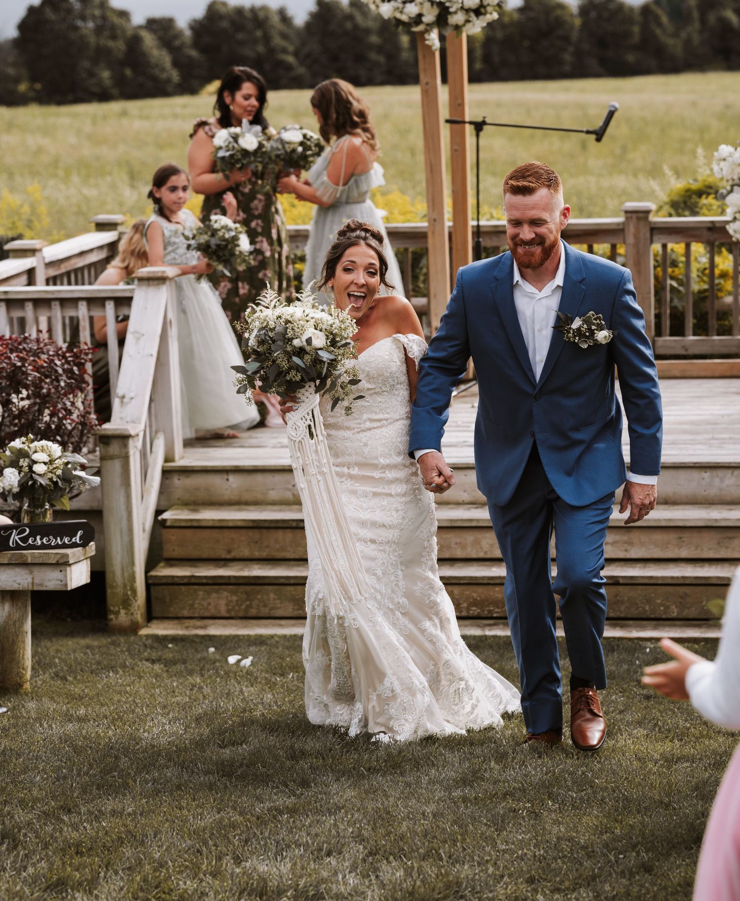 Joyful bride and groom walk back down the aisle at outdoor summer wedding ceremony.