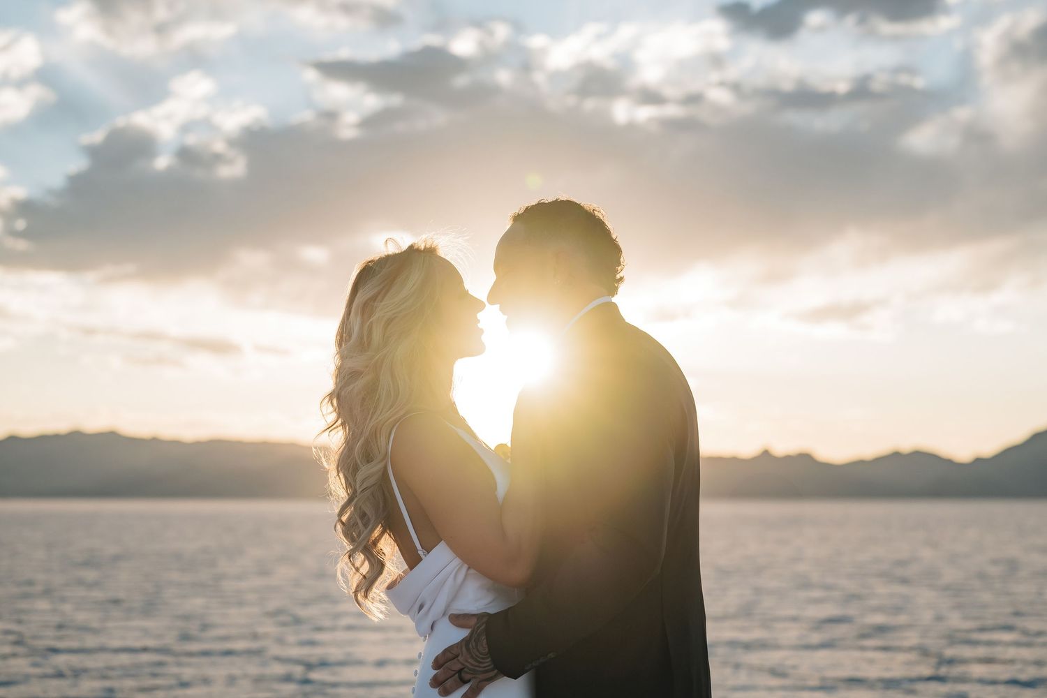 Romantic couple sharing a sunset kiss on salt flats, silhouetted against golden light and dramatic clouds.