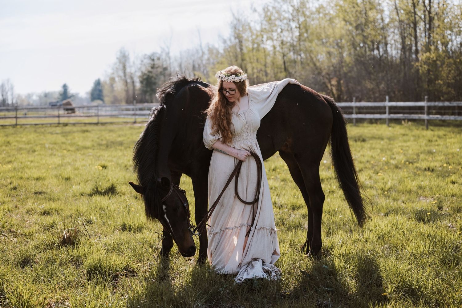 Elegant woman in a gown and floral crown poses with her horse outdoors.