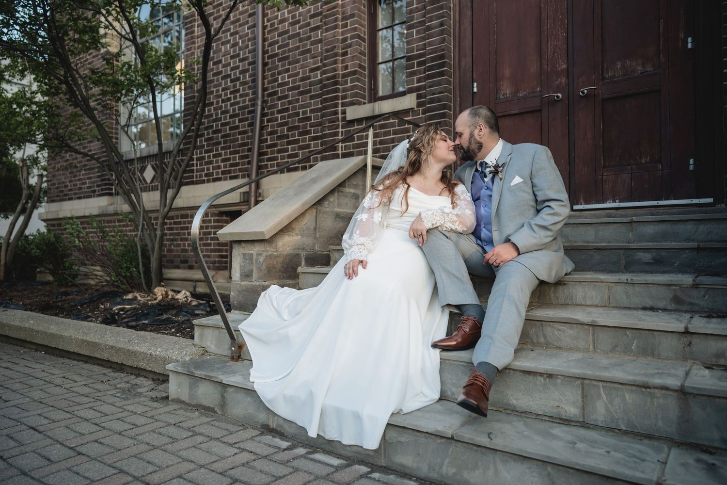 Bride and groom sitting on church steps, sharing a romantic moment in wedding attire, white gown flowing gracefully.