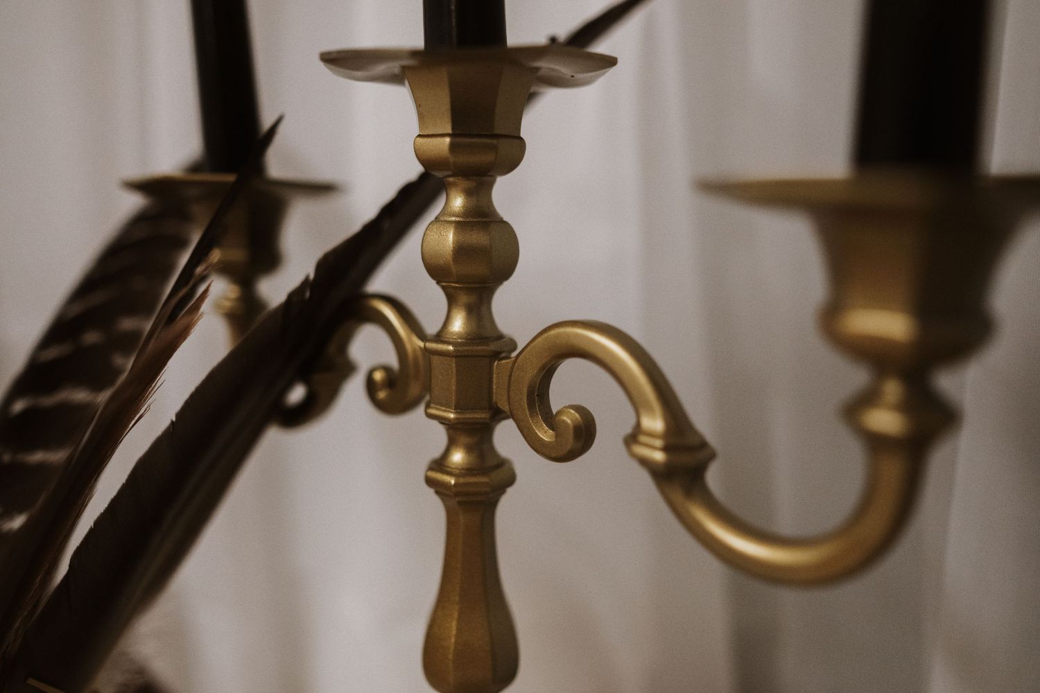 Close-up of ornate brass candelabra with decorative scrollwork against white backdrop.