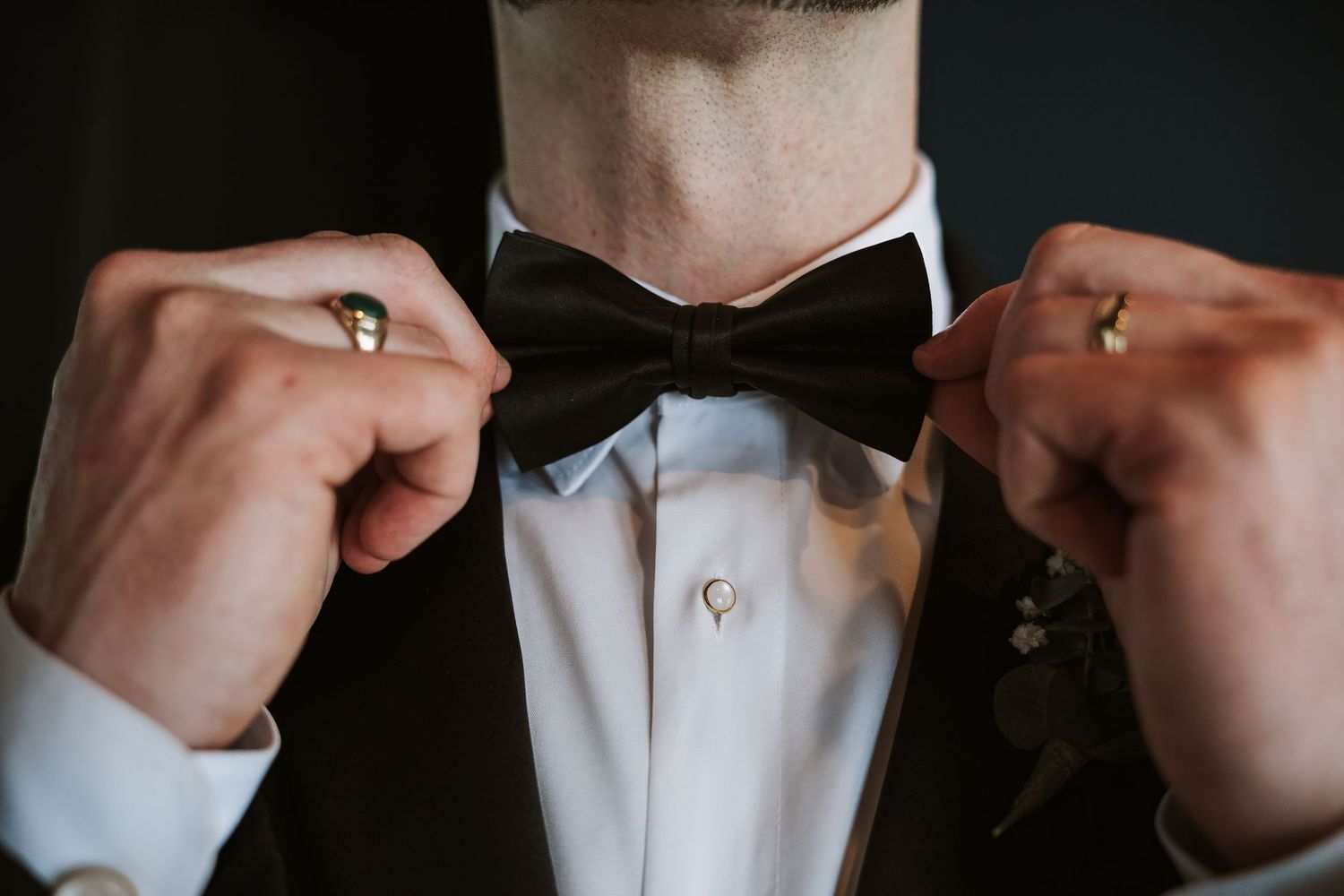 Groom adjusting black bow tie with both hands wearing formal tuxedo with boutonniere.