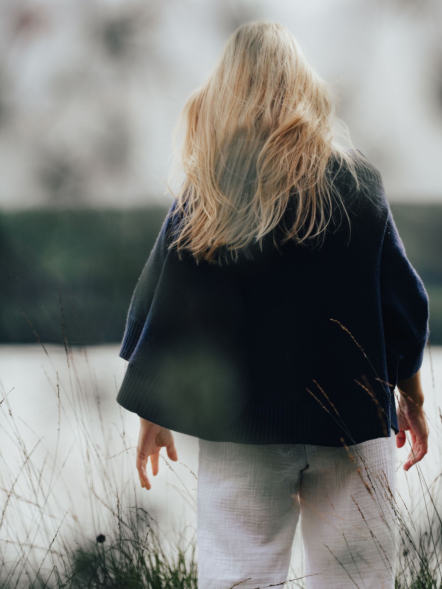 Artistic shot of a person walking through tall grass wearing dark top and white pants. For Ava Innes.