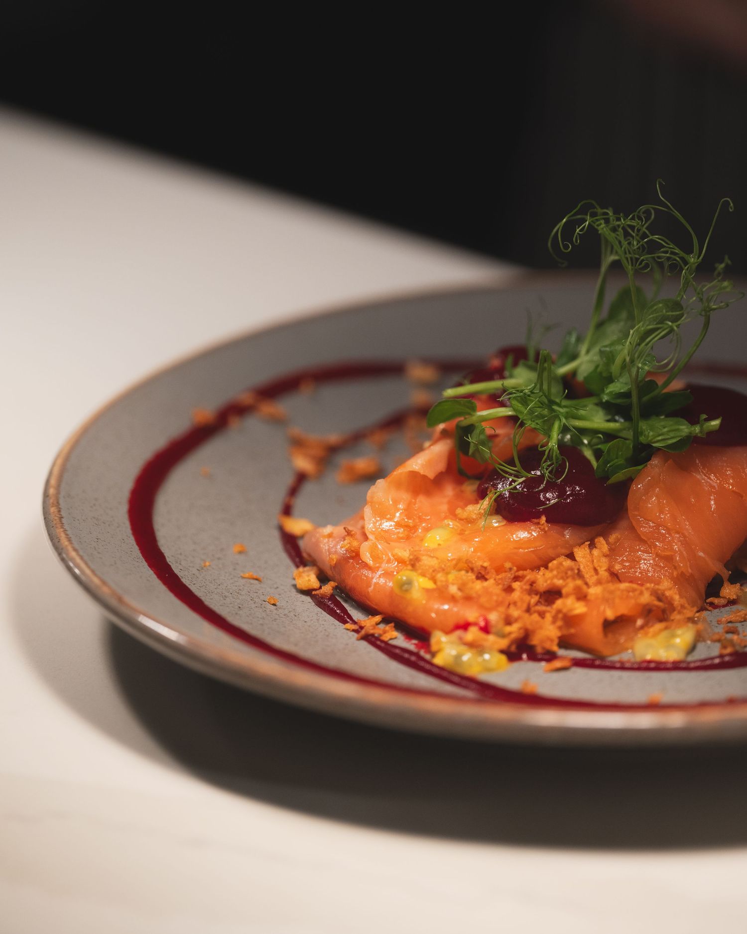 Elegantly plated salmon dish with red sauce and fresh herbs on a gray ceramic plate. Little Tuscany, Glasgow.