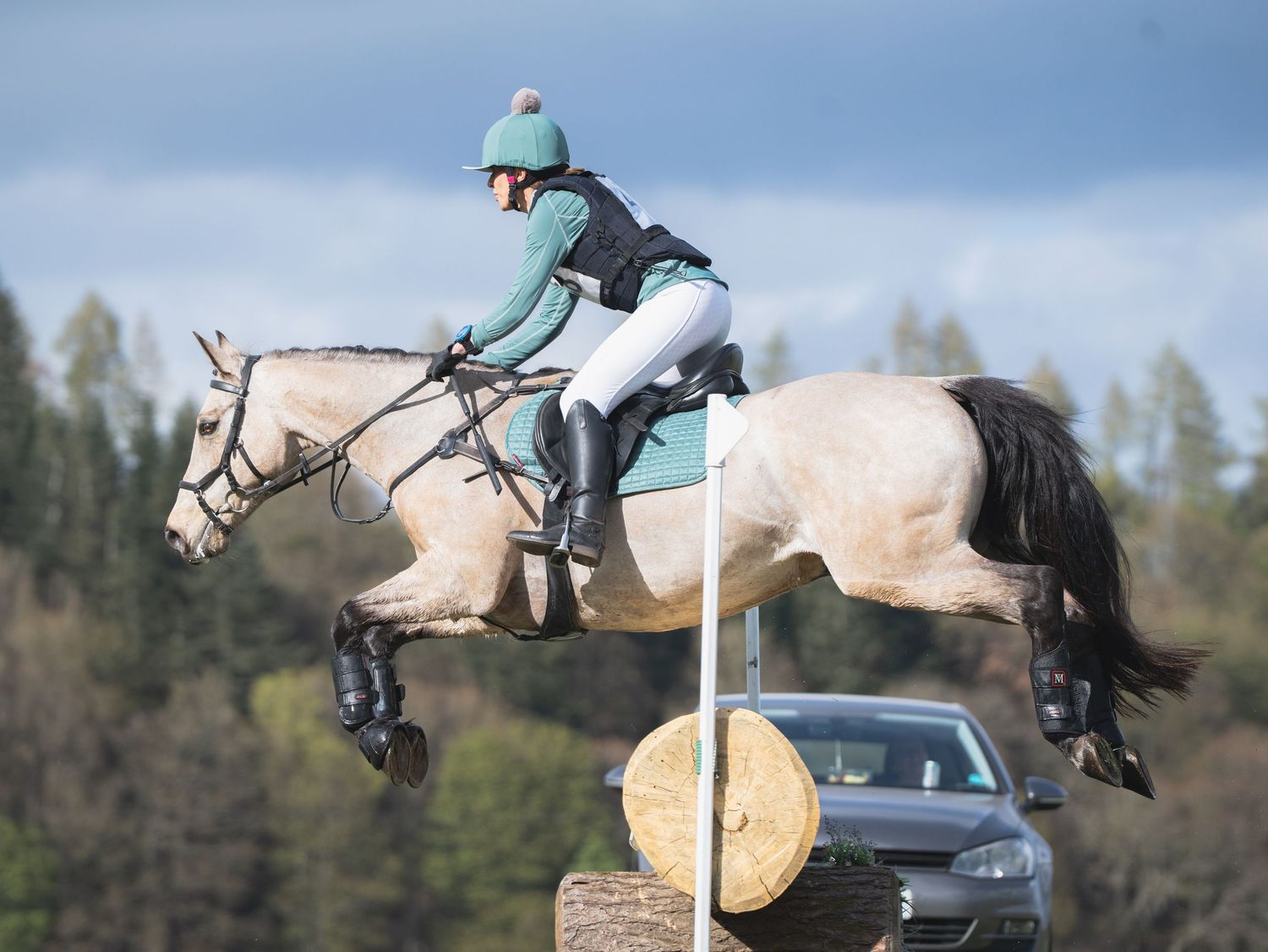 Equestrian jumping over a log obstacle on a white horse during competition.