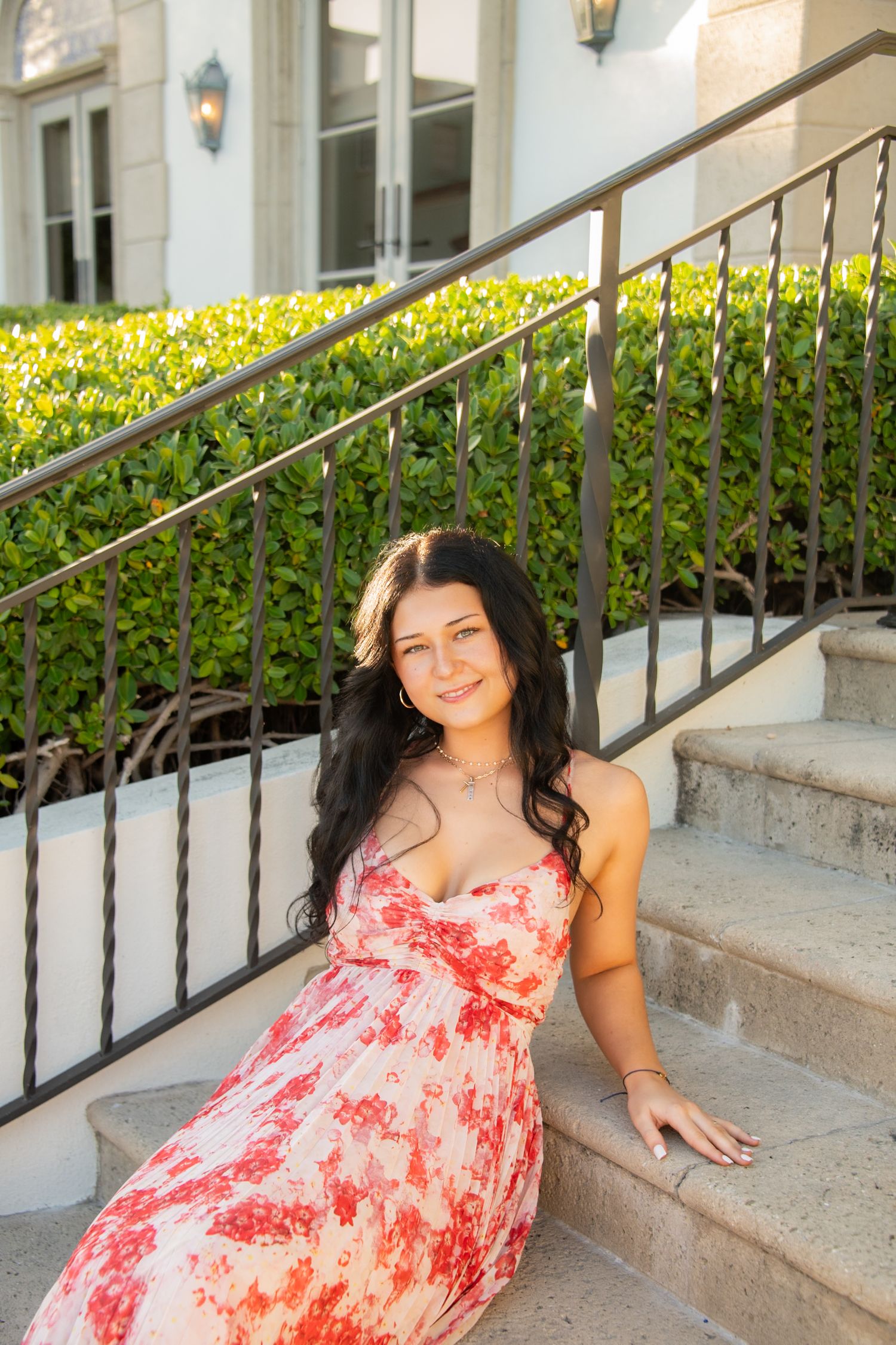 A person in a coral floral sundress sits on outdoor stone steps next to decorative railings and greenery.