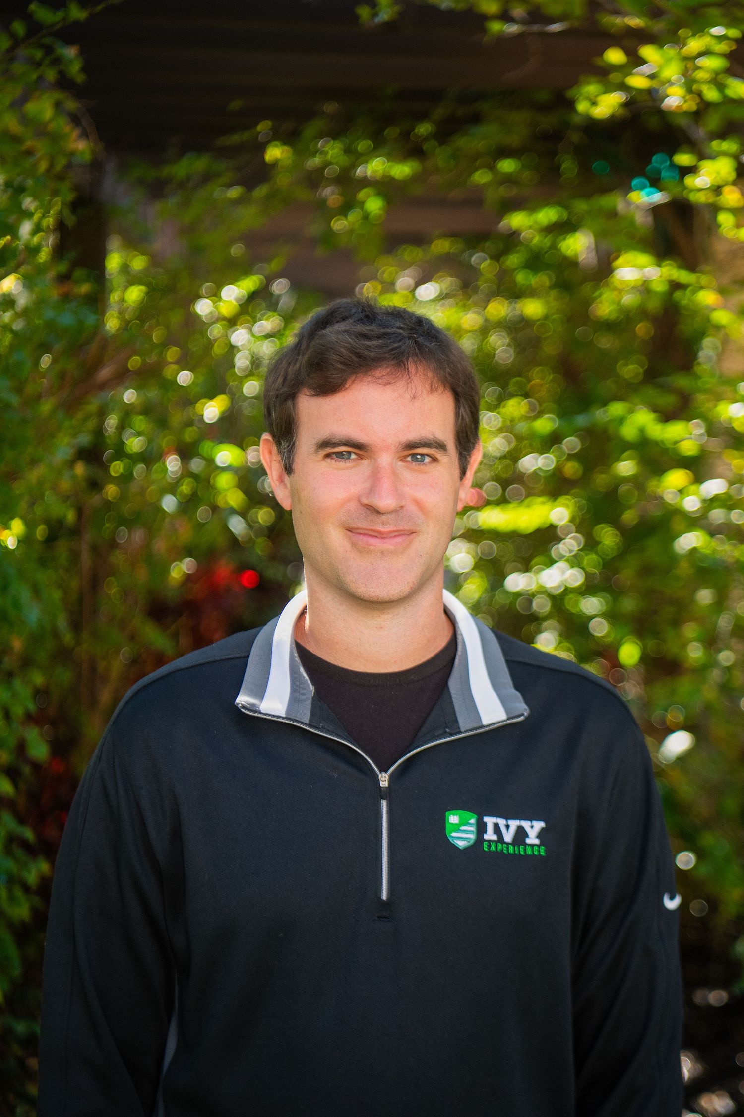 A person wearing a black zip-up jacket smiles against a green leafy background in a series of similar photos.