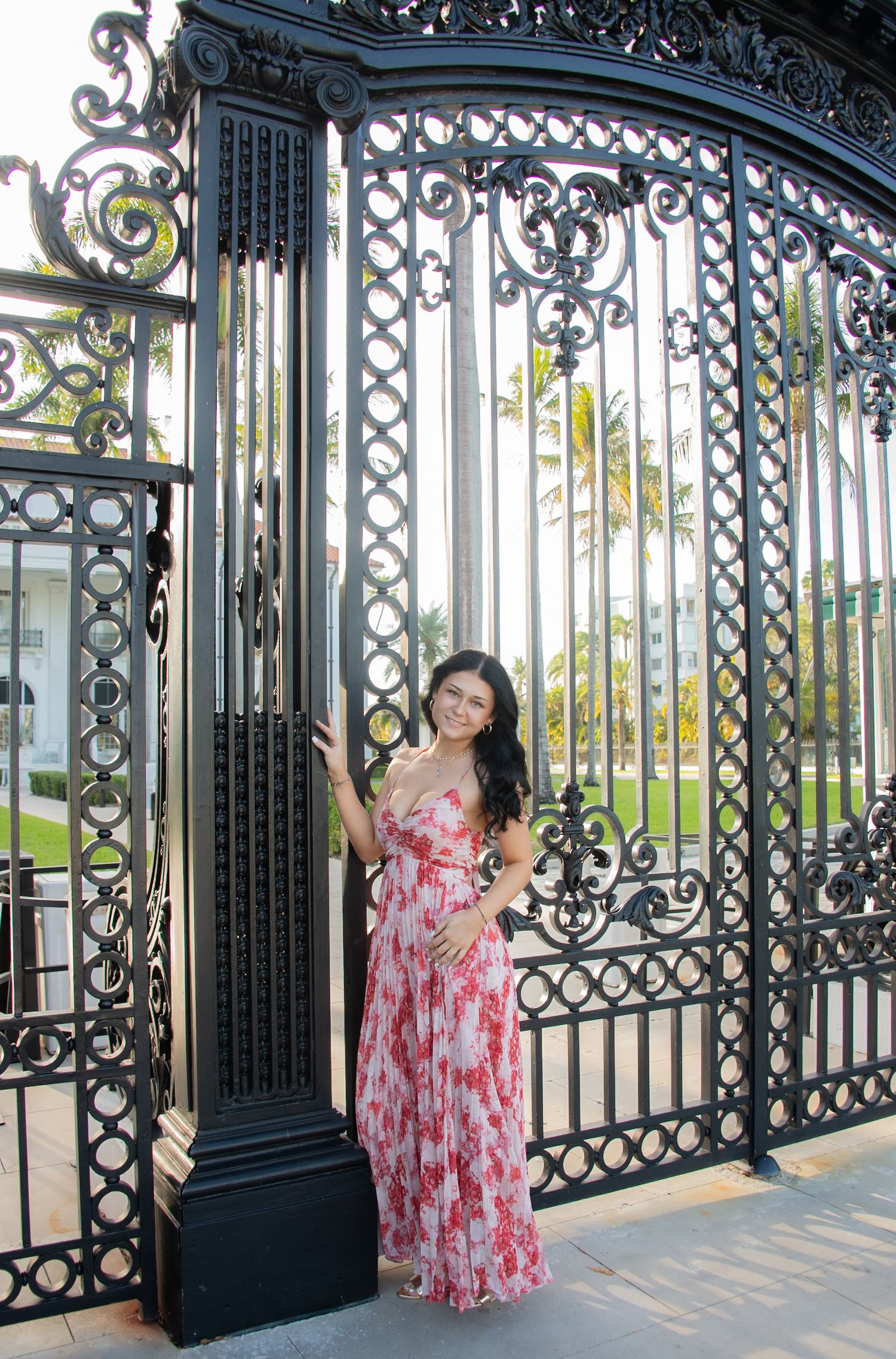 A person in a pink floral dress poses playfully at ornate black iron gates in a series of four connected photos.