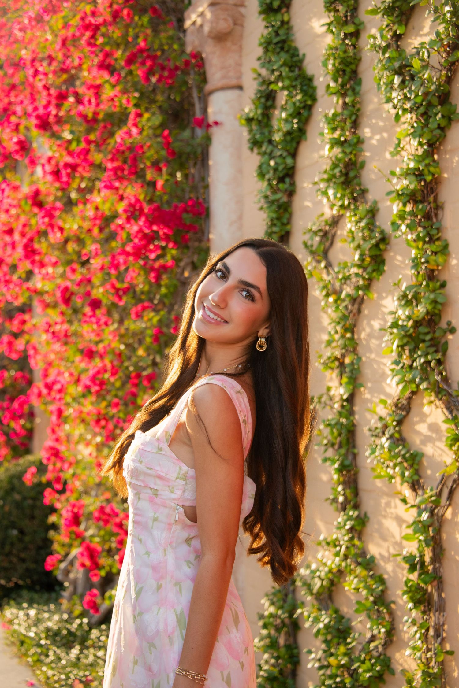 A dreamy outdoor portrait against a wall covered in vibrant pink bougainvillea flowers and green vines.