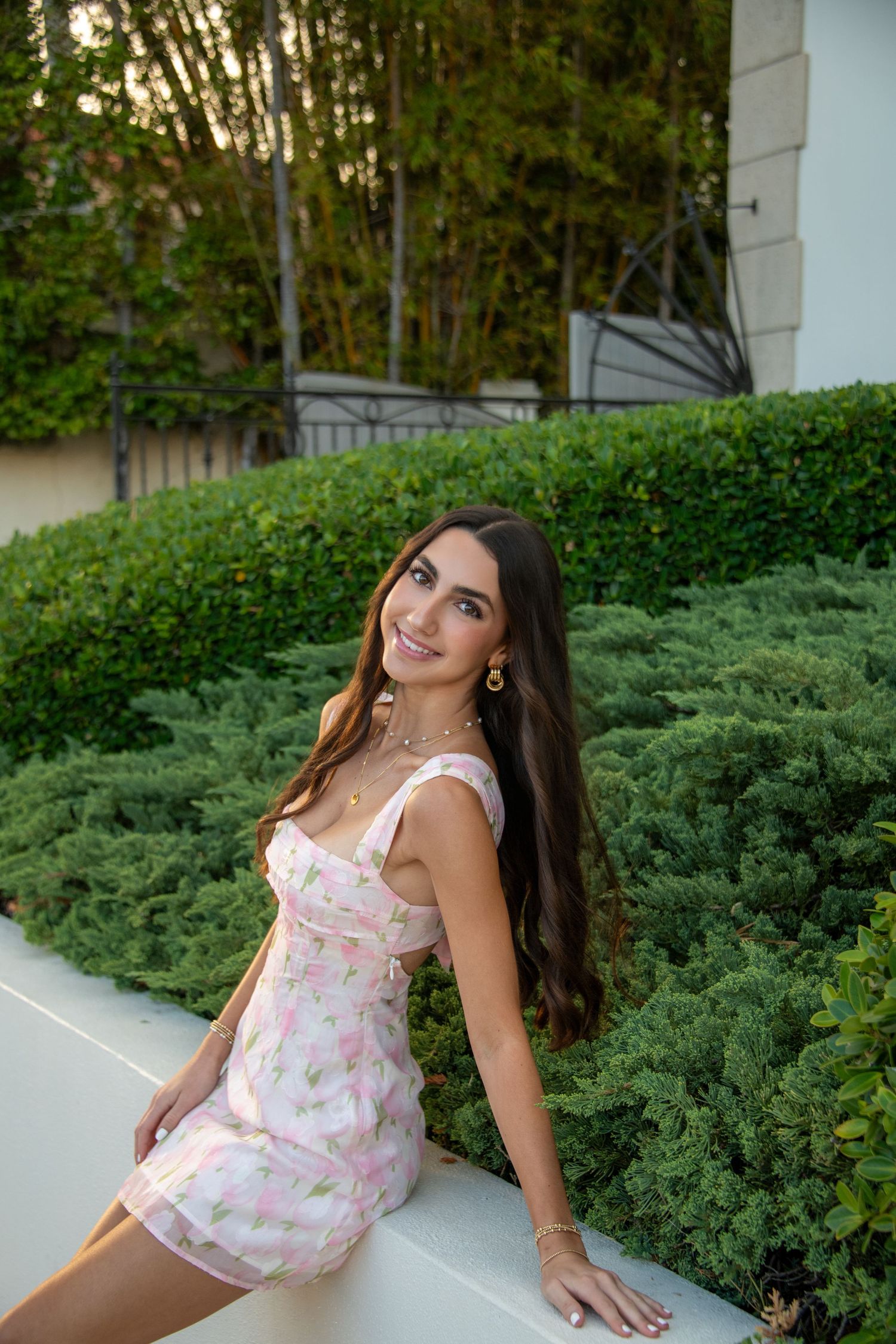 A series of outdoor portrait photos featuring someone in a floral dress posing against greenery and architectural elements.