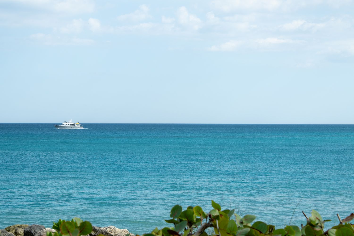 Turquoise ocean waters meet the horizon with a small boat visible in the distance under clear blue skies.