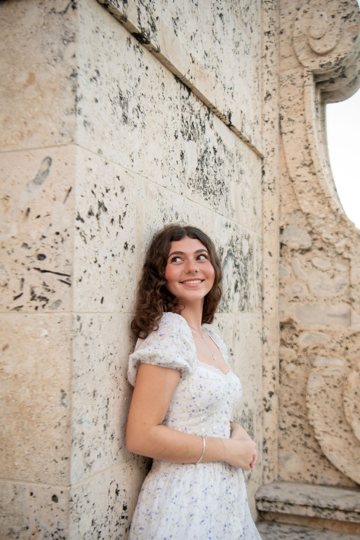 A person in a white lace dress poses against a textured stone wall in an artistic photo series.