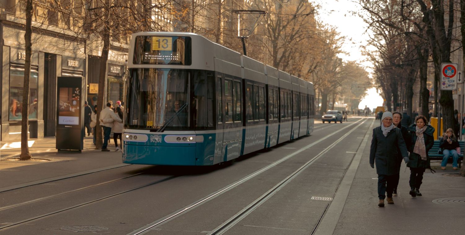 Urban street scene with tram tracks and bare trees lining a wide boulevard.