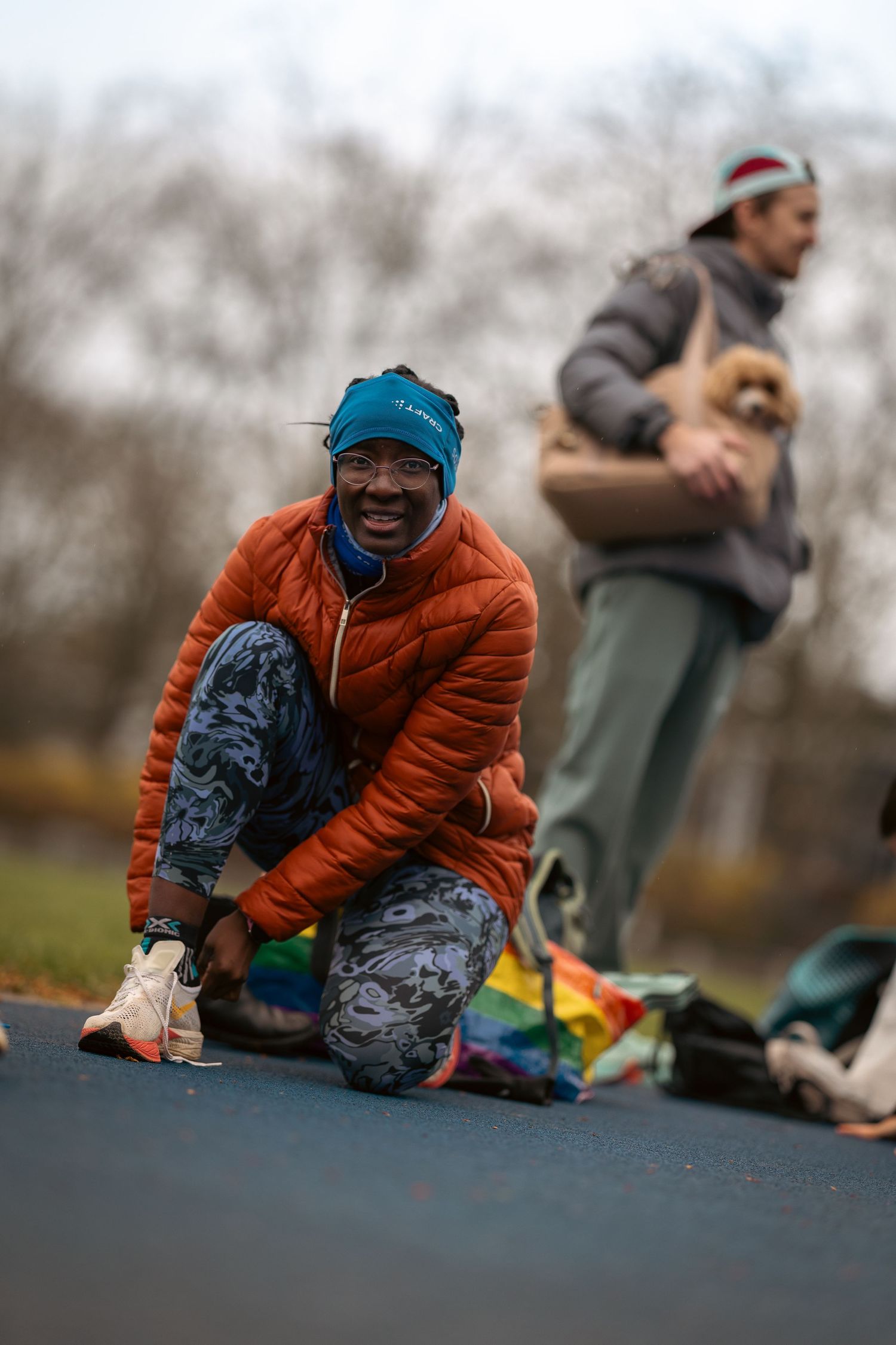 Person in orange jacket and patterned pants crouches on outdoor track during athletic activity.