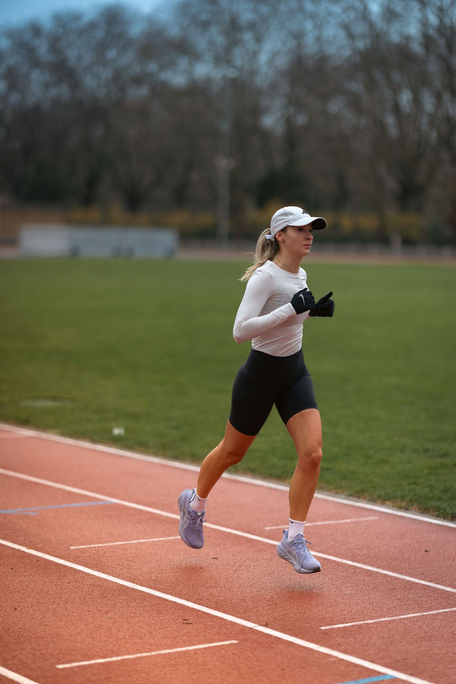 Runner in white top and navy shorts practicing sprints on red track surface.