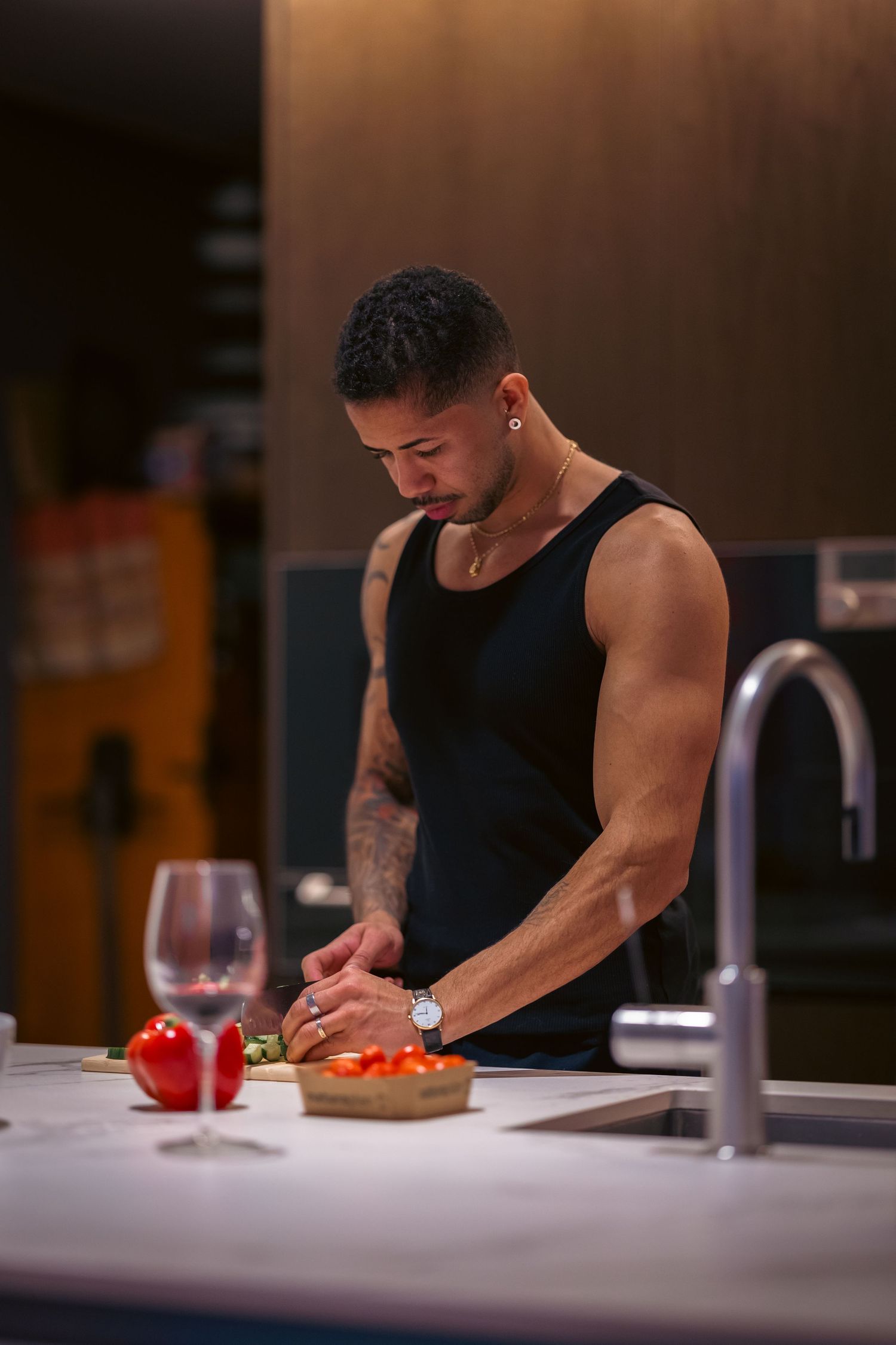 A muscular man in a black tank top chopping vegetables at a modern kitchen counter.