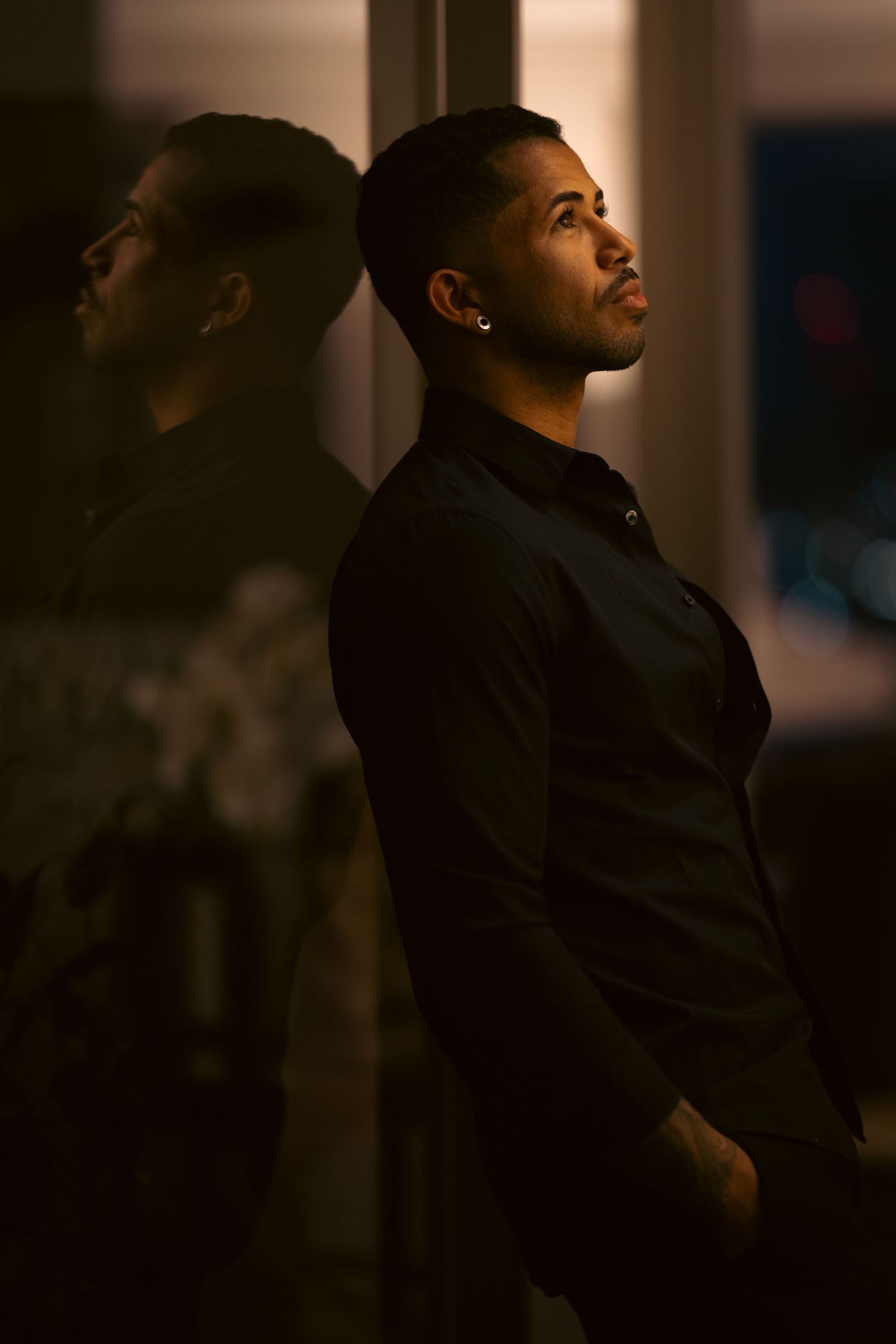 A silhouetted figure gazes upward in a dimly lit room, creating a dramatic profile against the dark background.