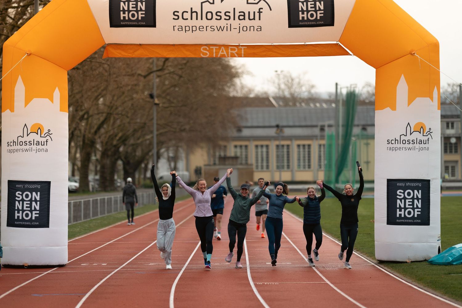 Group of runners celebrating at finish line under branded event banner.