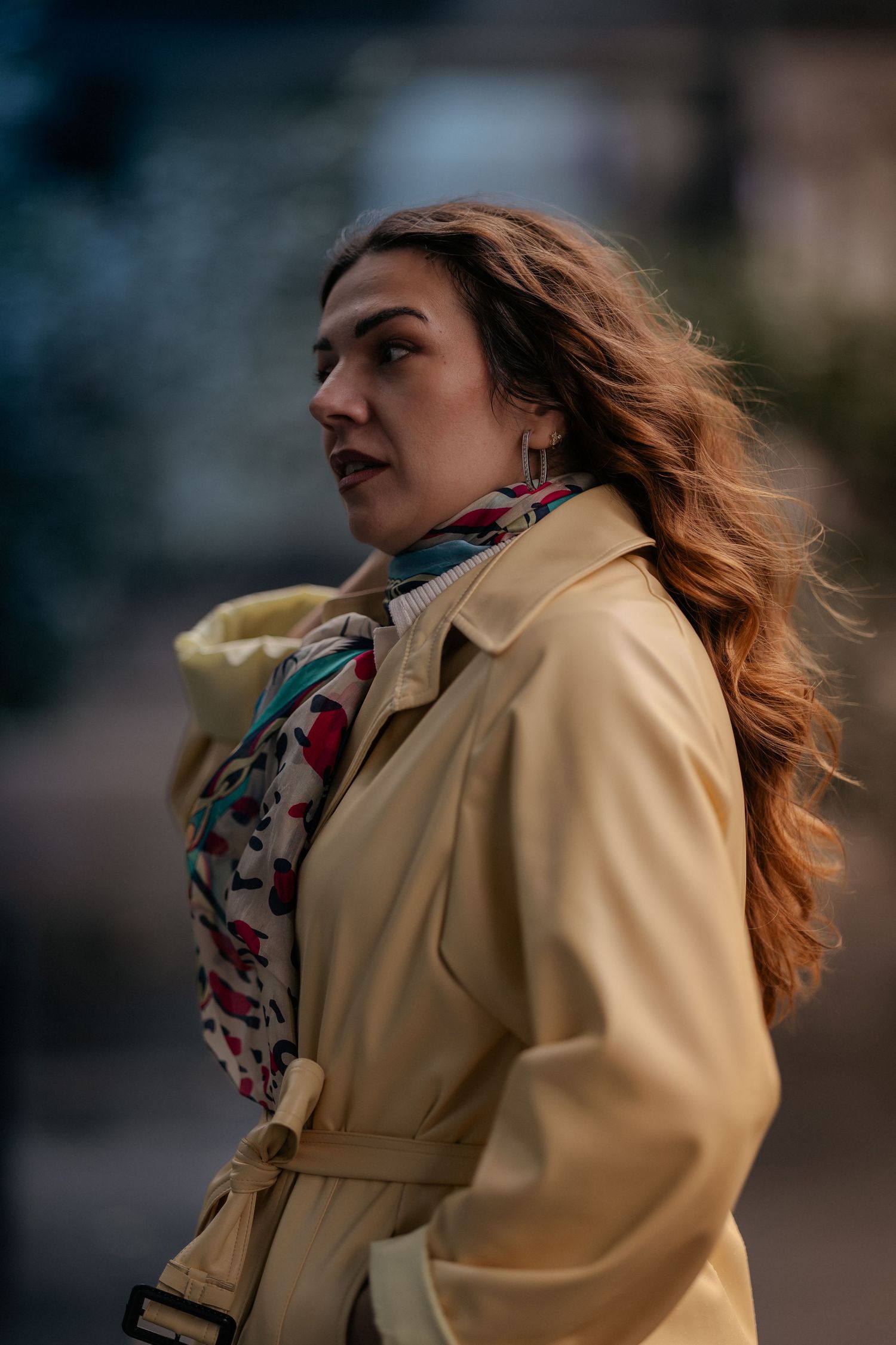 A person in a yellow coat and patterned scarf shown in a sequence of windy outdoor portraits.