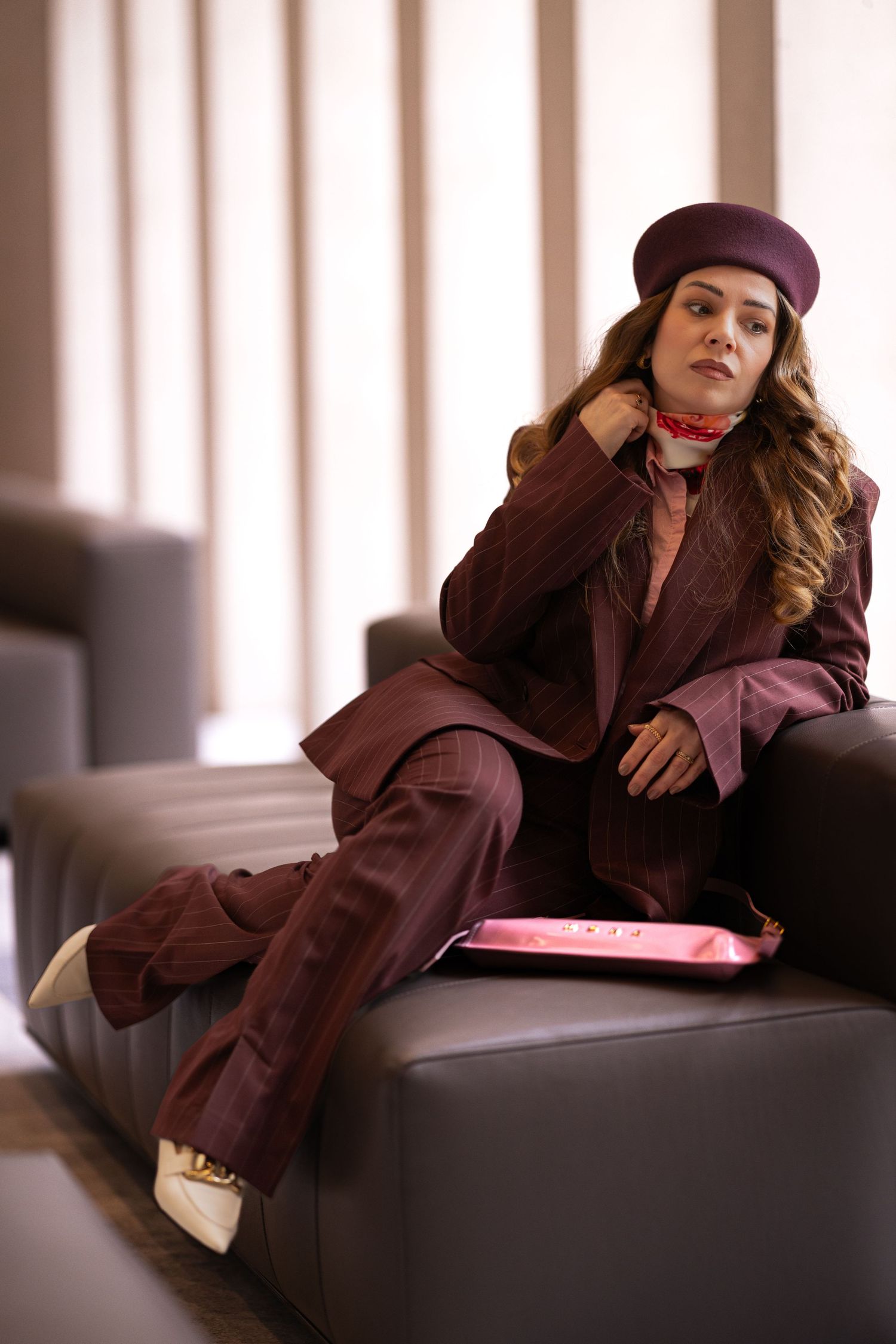 A person in a brown coat and beret poses on a leather couch in a series of artistic fashion photographs.