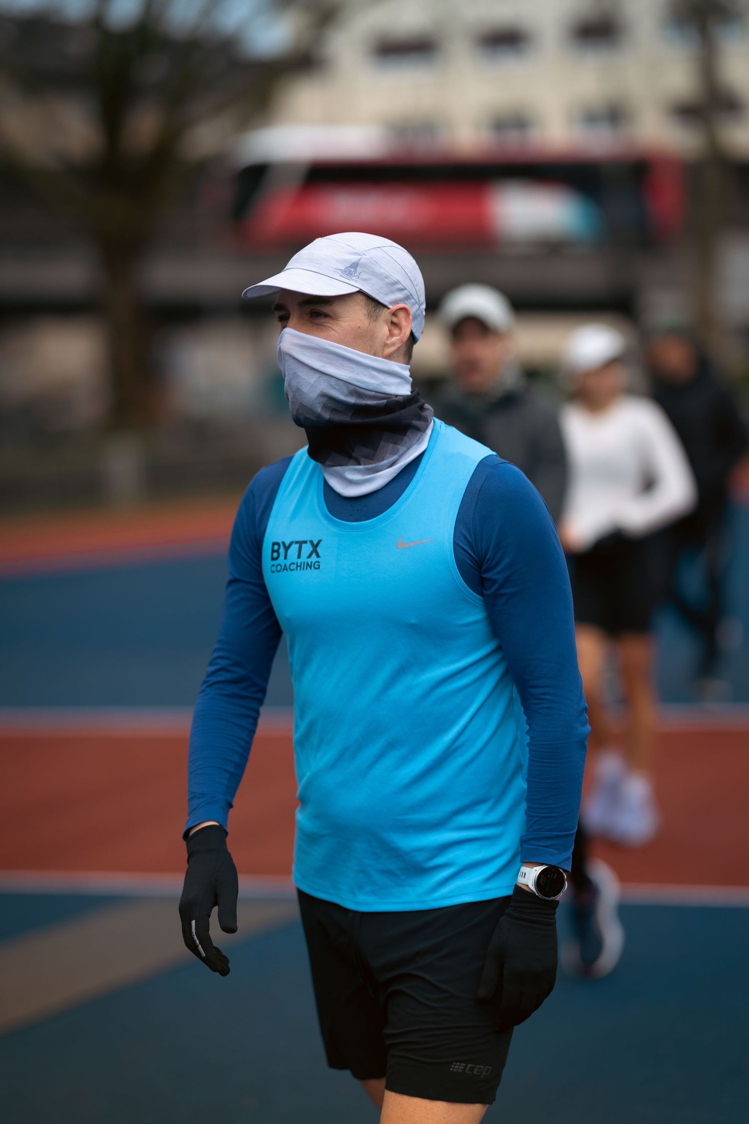Runner wearing a light blue long sleeve shirt and black shorts exercising on an outdoor track.