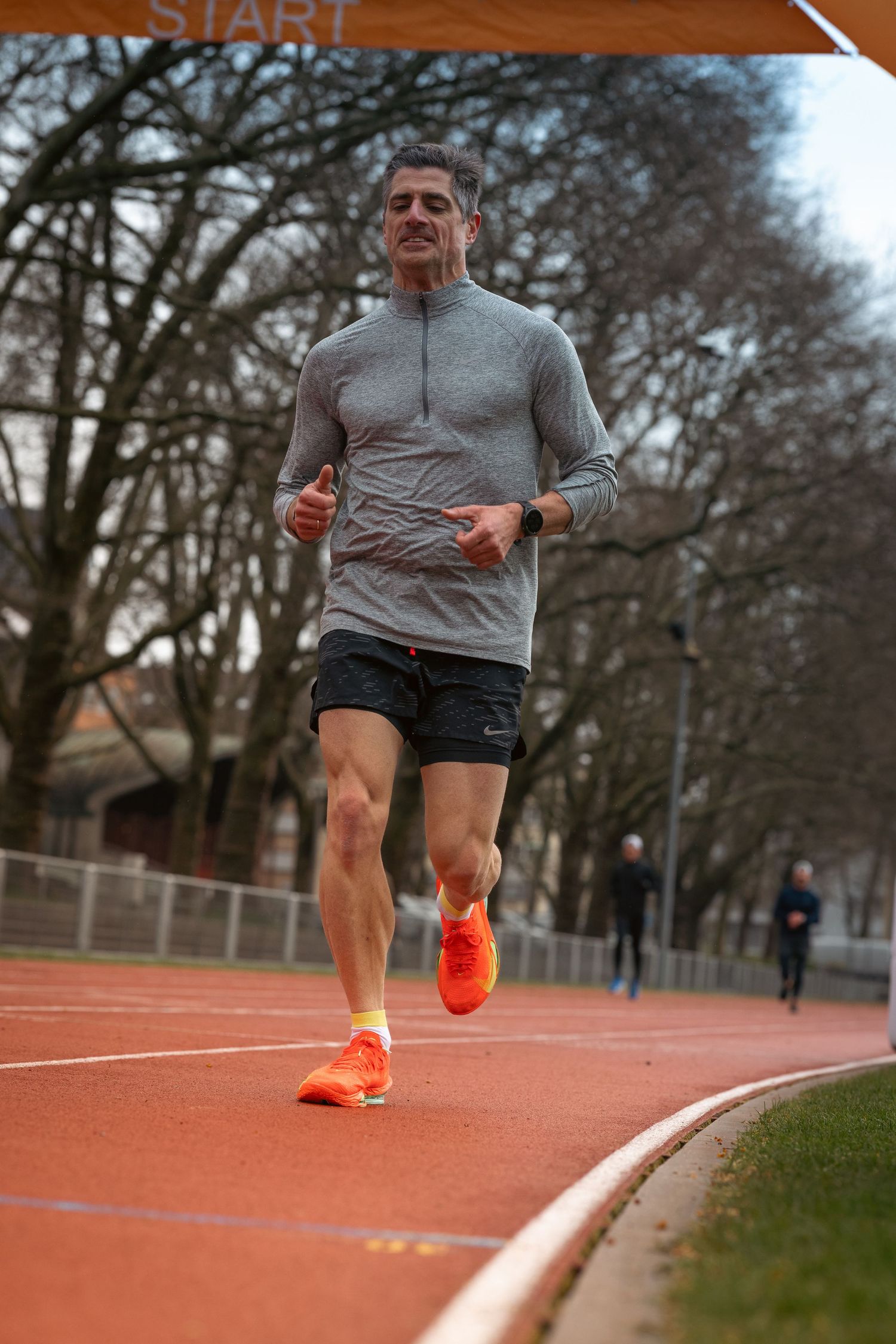 Runner in grey top and black shorts training on an orange running track.