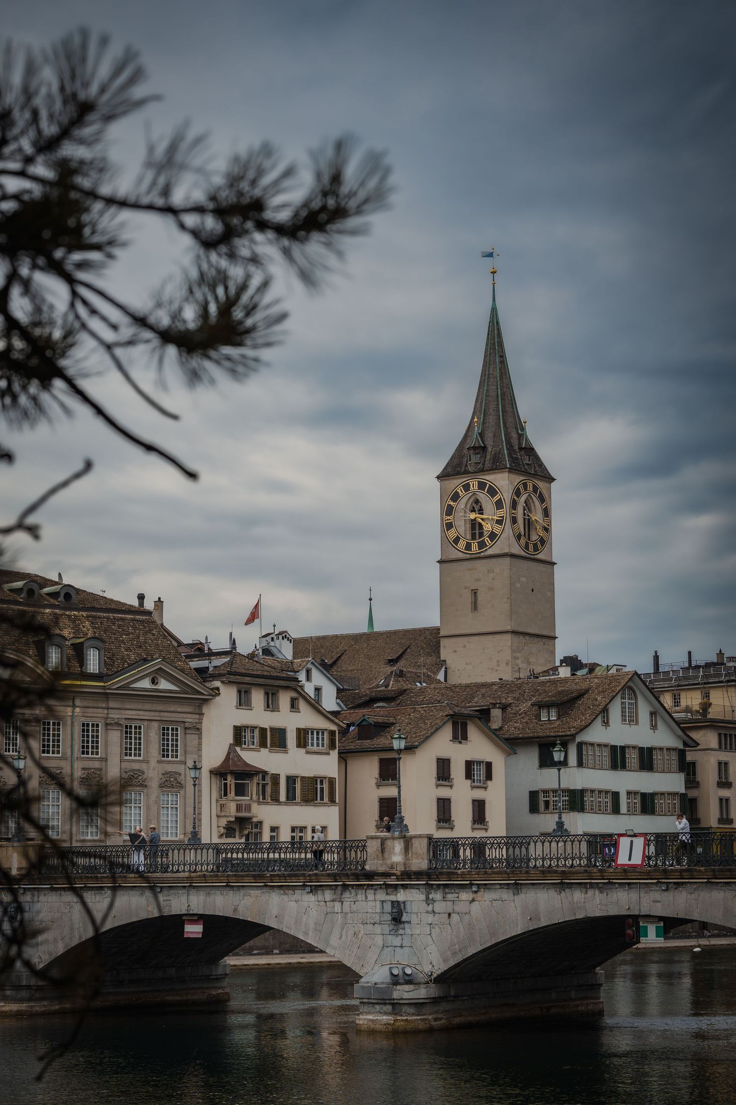 Historic Zurich skyline with St. Peter Church clock tower rising above old town buildings along the Limmat River bridge.