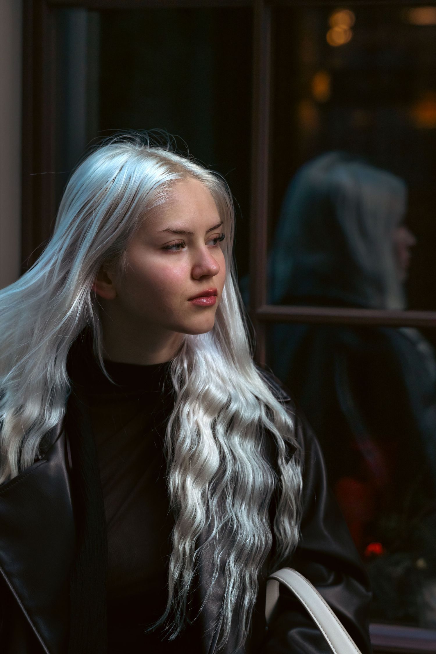 Portrait of a person with flowing platinum white wavy hair wearing a black top in moody lighting.