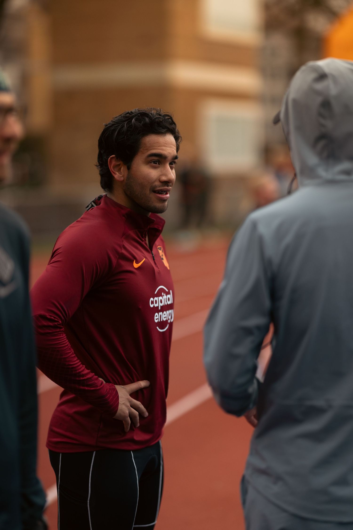 Coach in maroon athletic wear leading a training session on an outdoor track.
