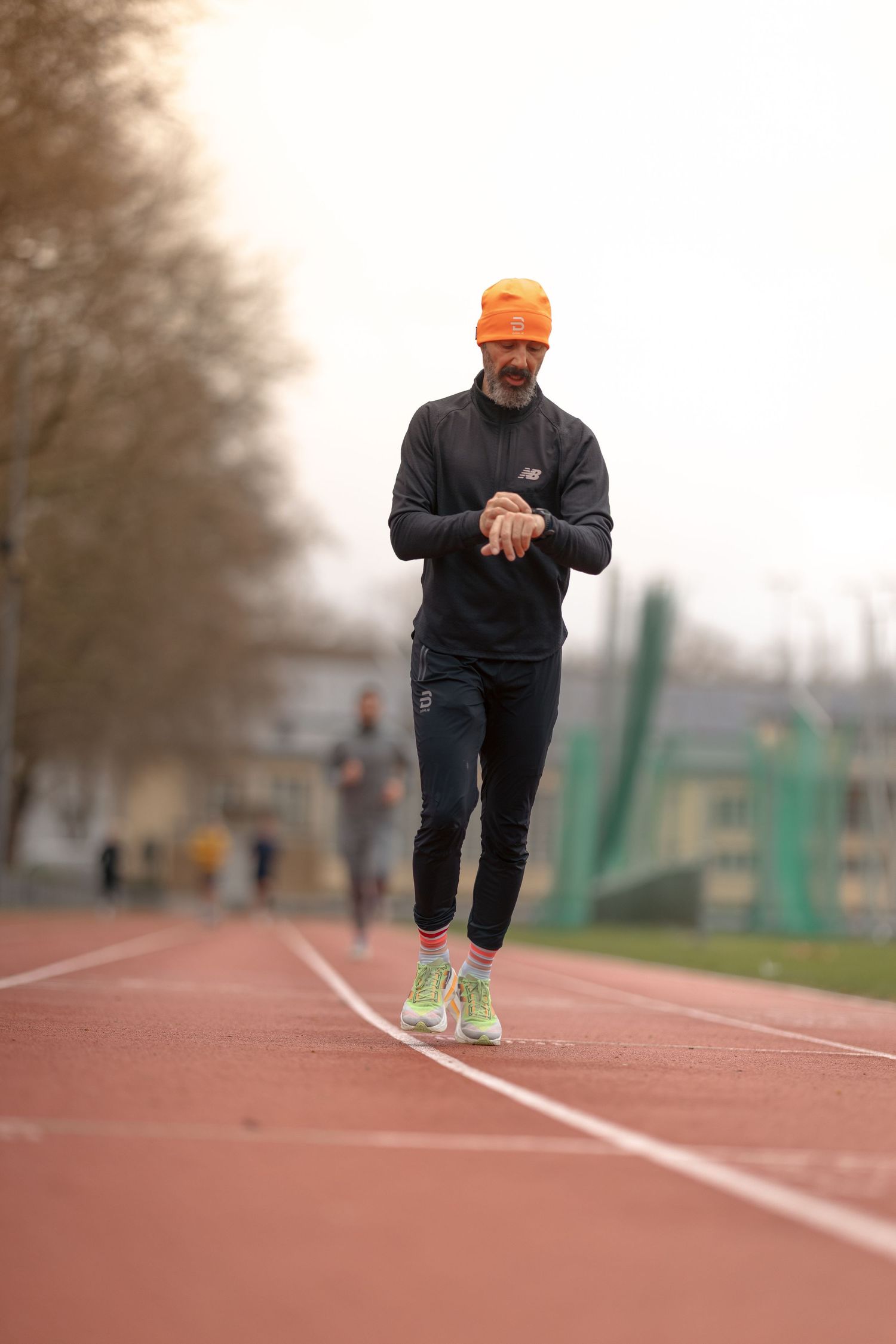 Runner practicing sprinting technique on red athletic track wearing dark athletic gear.