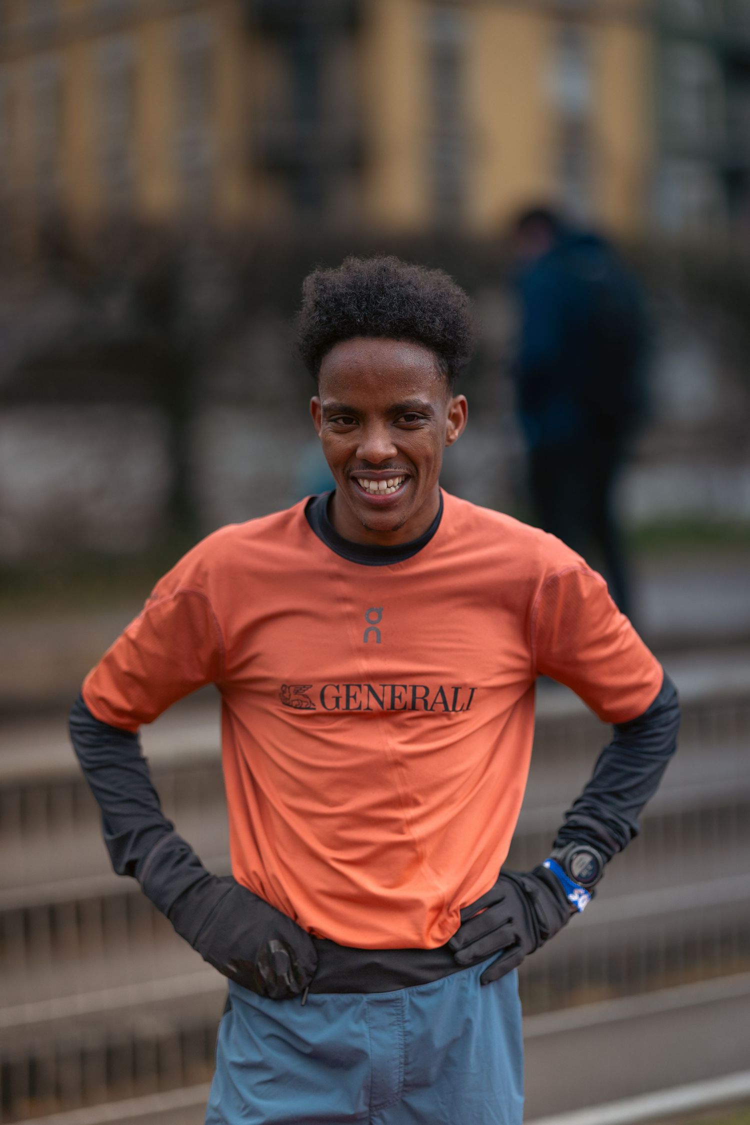 Athlete in orange shirt and dark sleeves smiling during outdoor training session.