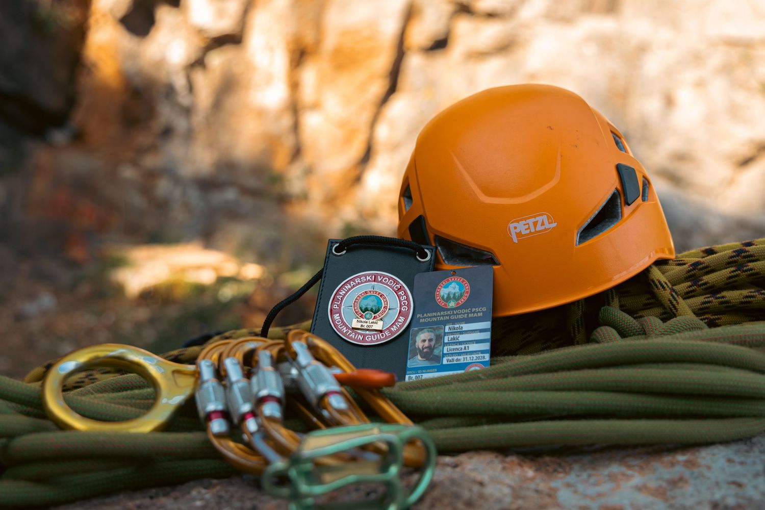 Orange Petzl climbing helmet with carabiners, rope, and gear patches on rocky surface.