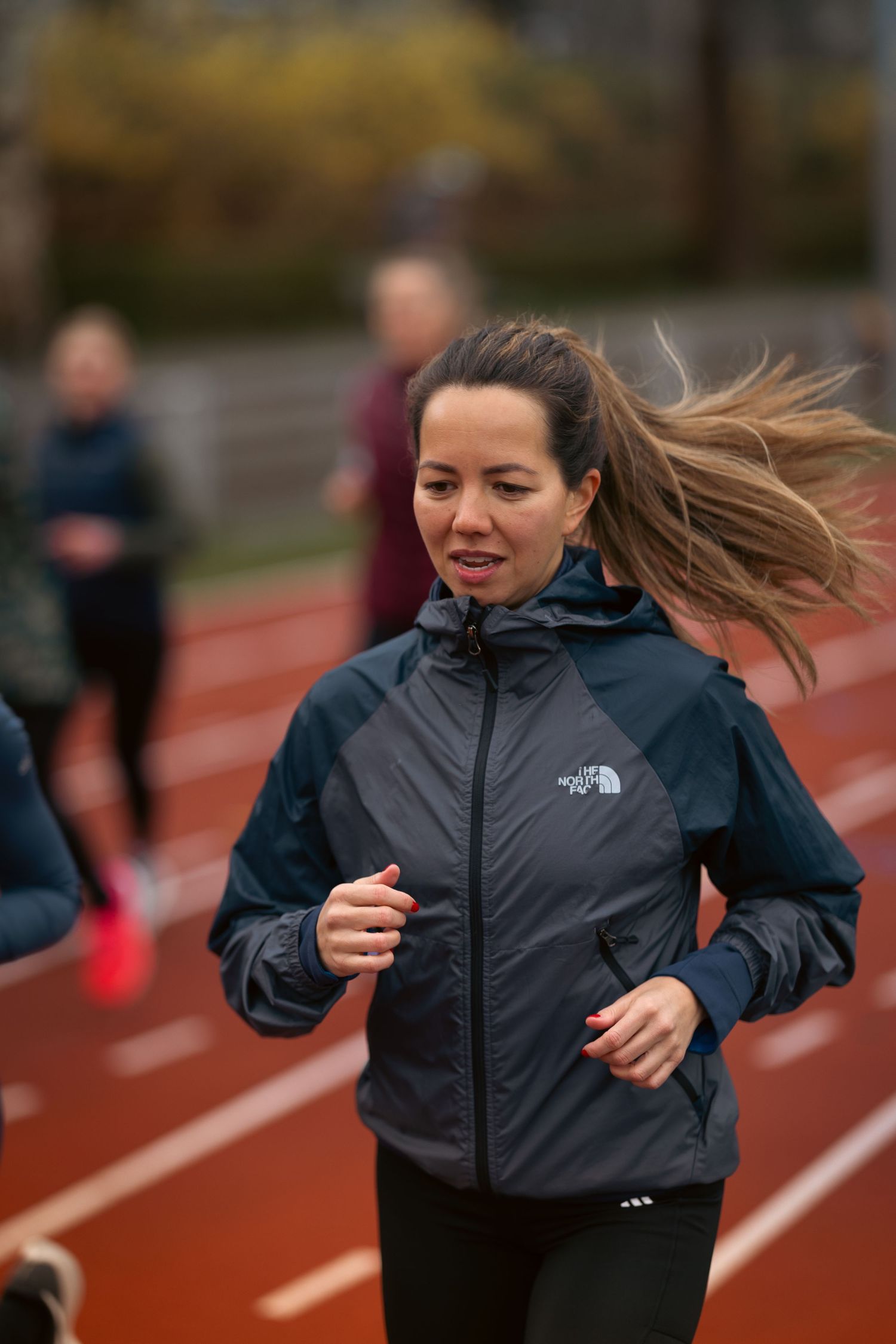 Runner in a North Face jacket sprinting on a red track during an outdoor training session.