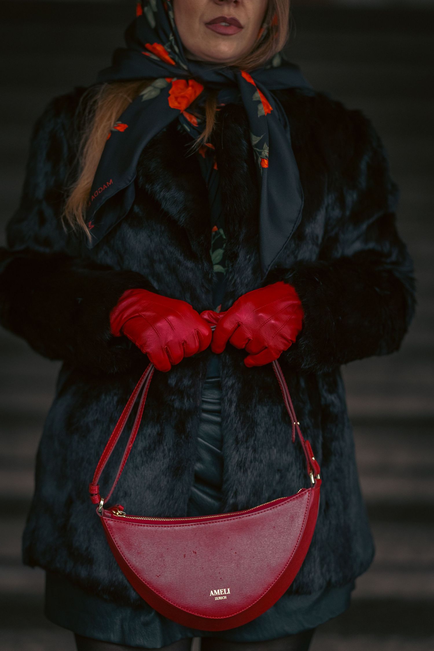 Woman in dark fur coat holding red ANELI Paris handbag, wearing red gloves and floral scarf.