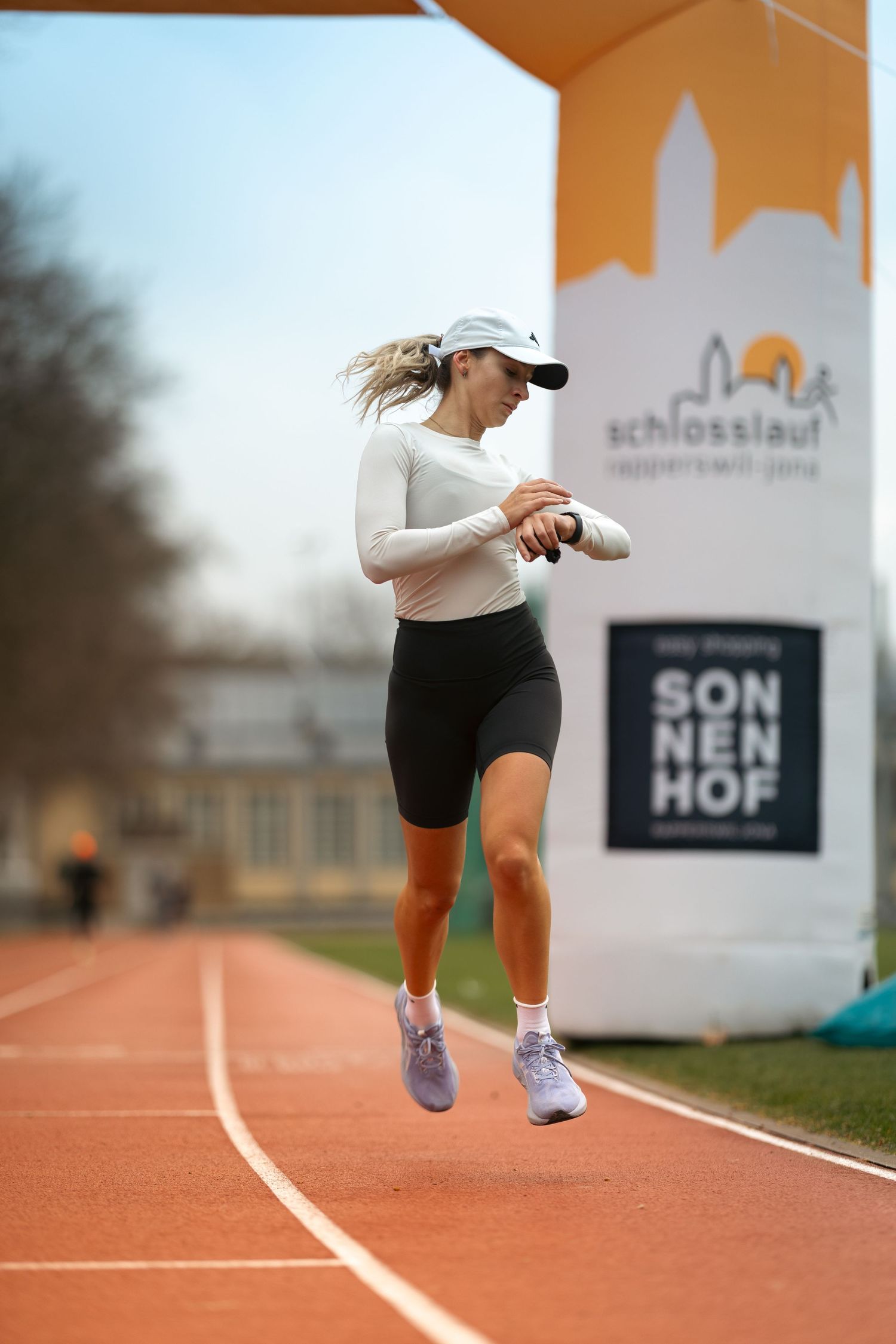 Athlete checking smartwatch while jumping on running track with event banner in background.