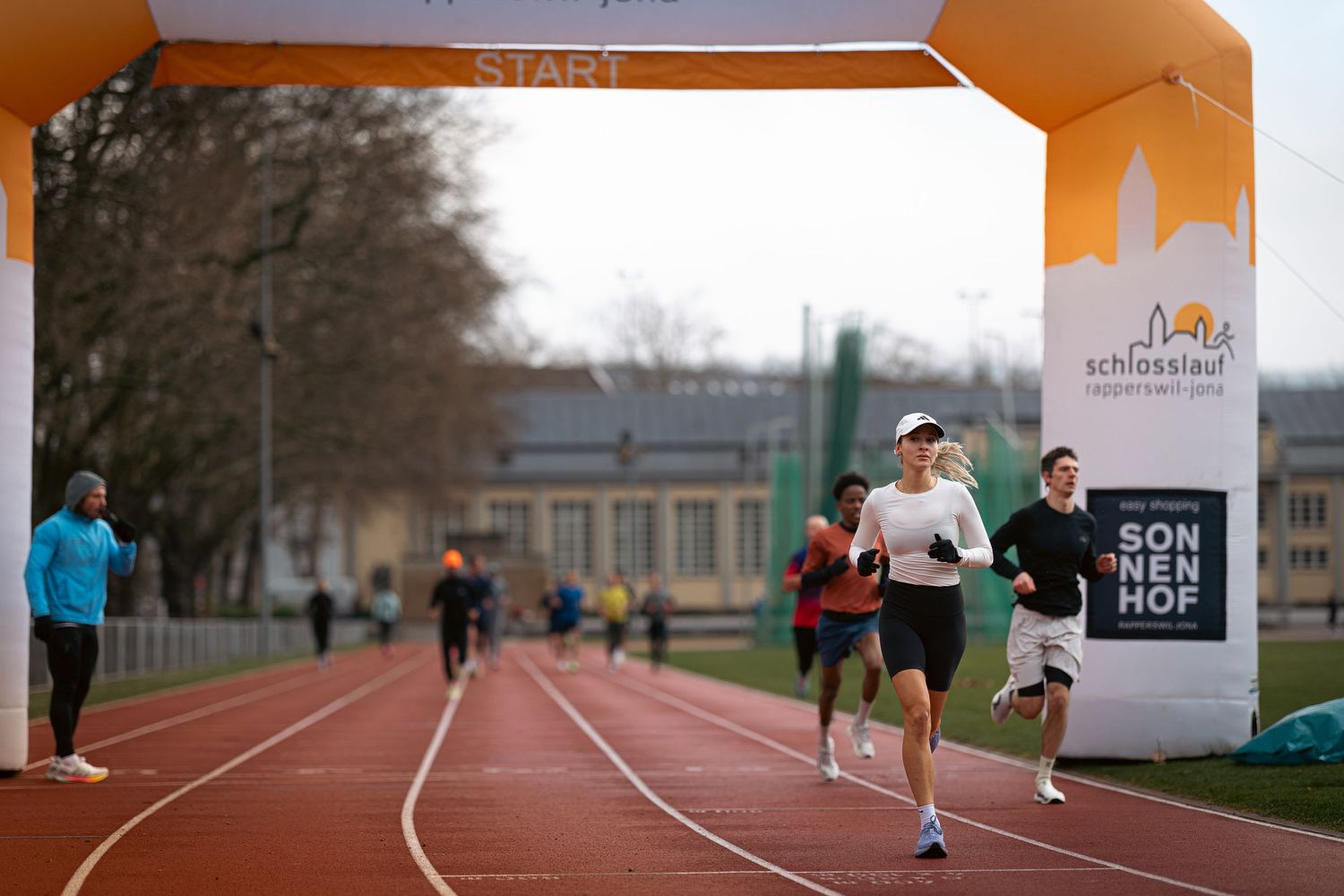 Runners training on an outdoor athletic track with orange markers visible.