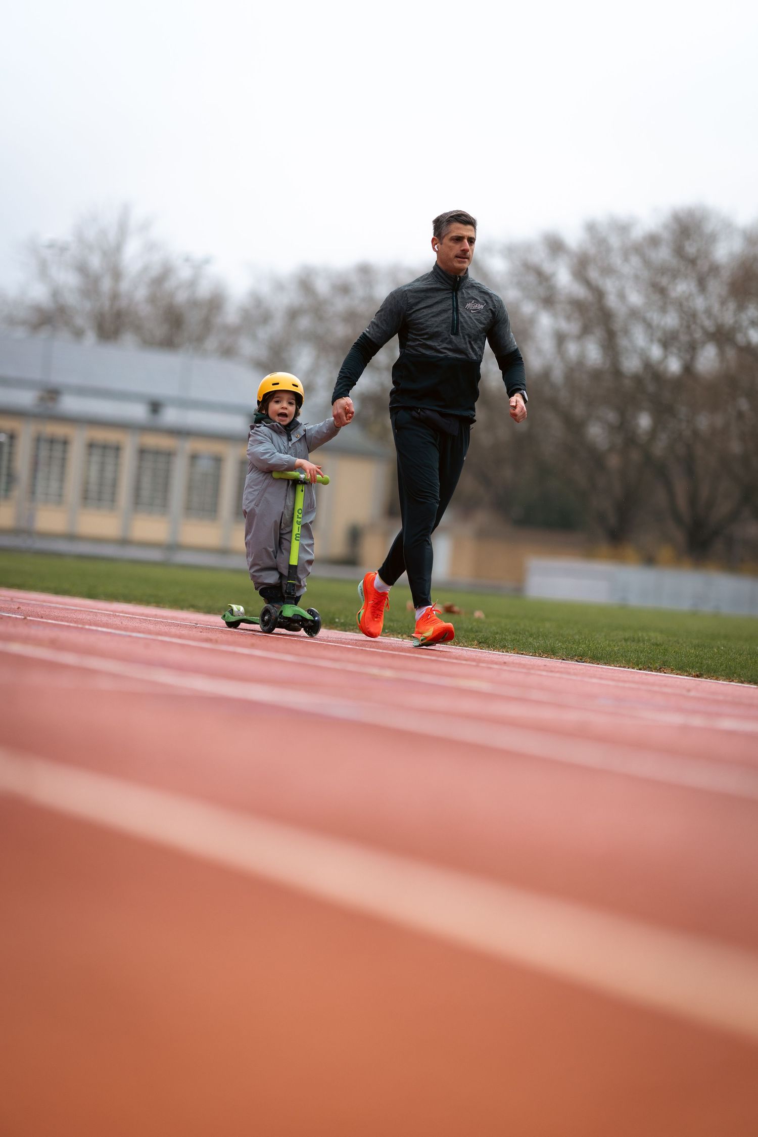 Athletes running on an outdoor track during a training session in overcast weather.
