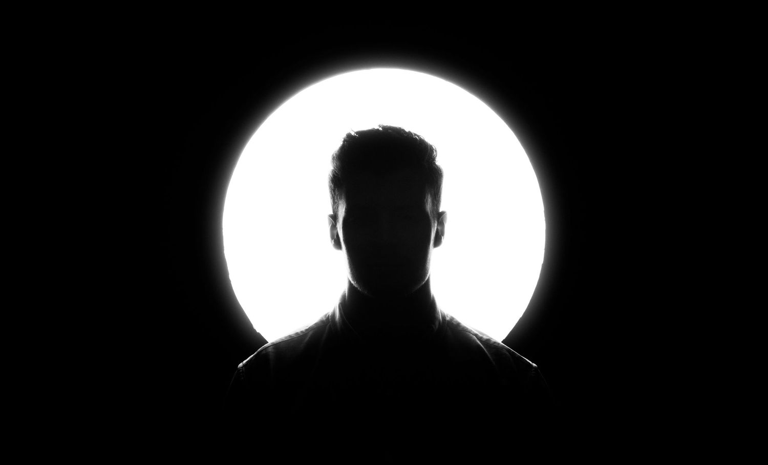 Silhouetted person against a bright circular white light on a dark black background.