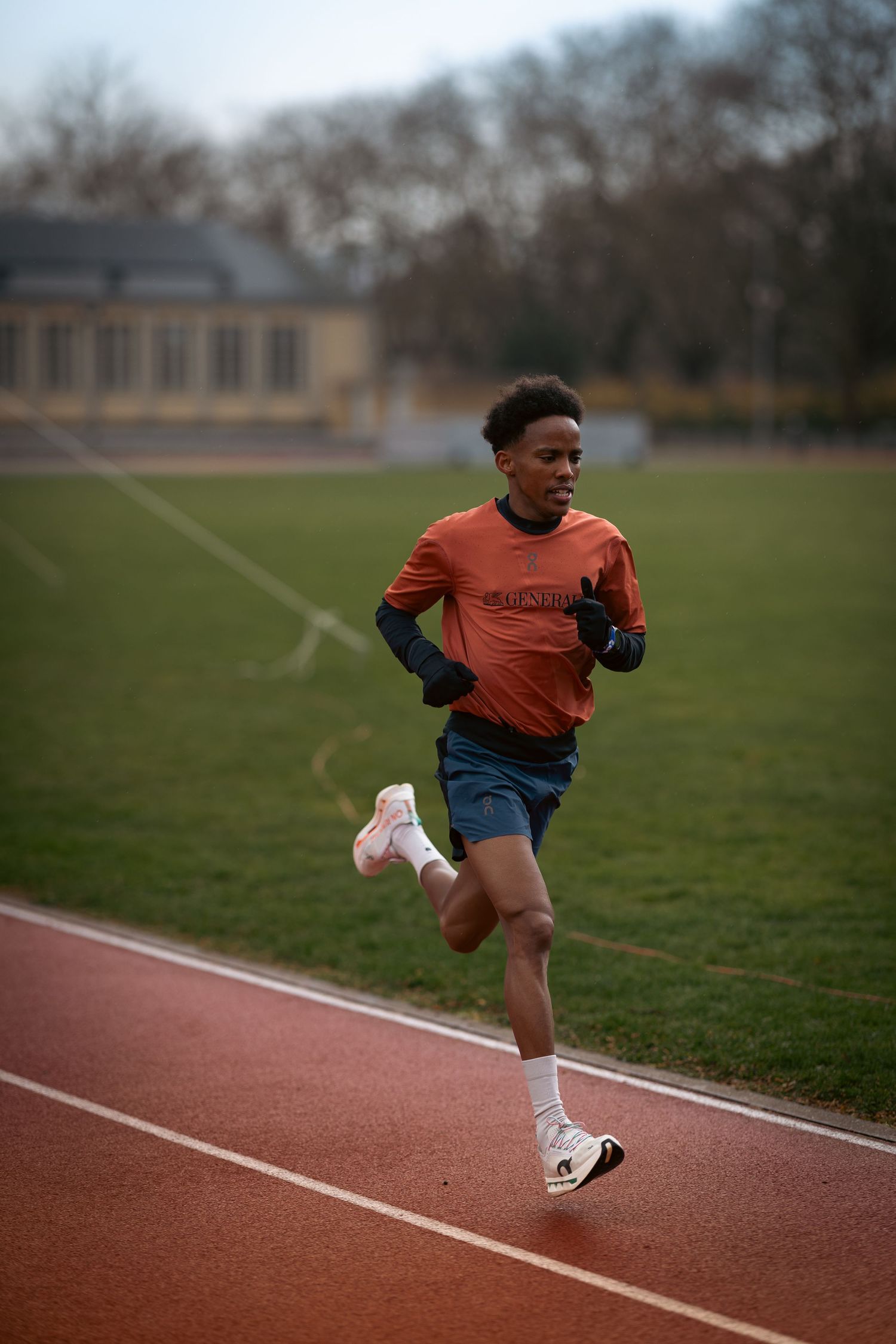 Runner in orange and navy athletic wear sprinting on a track during practice.