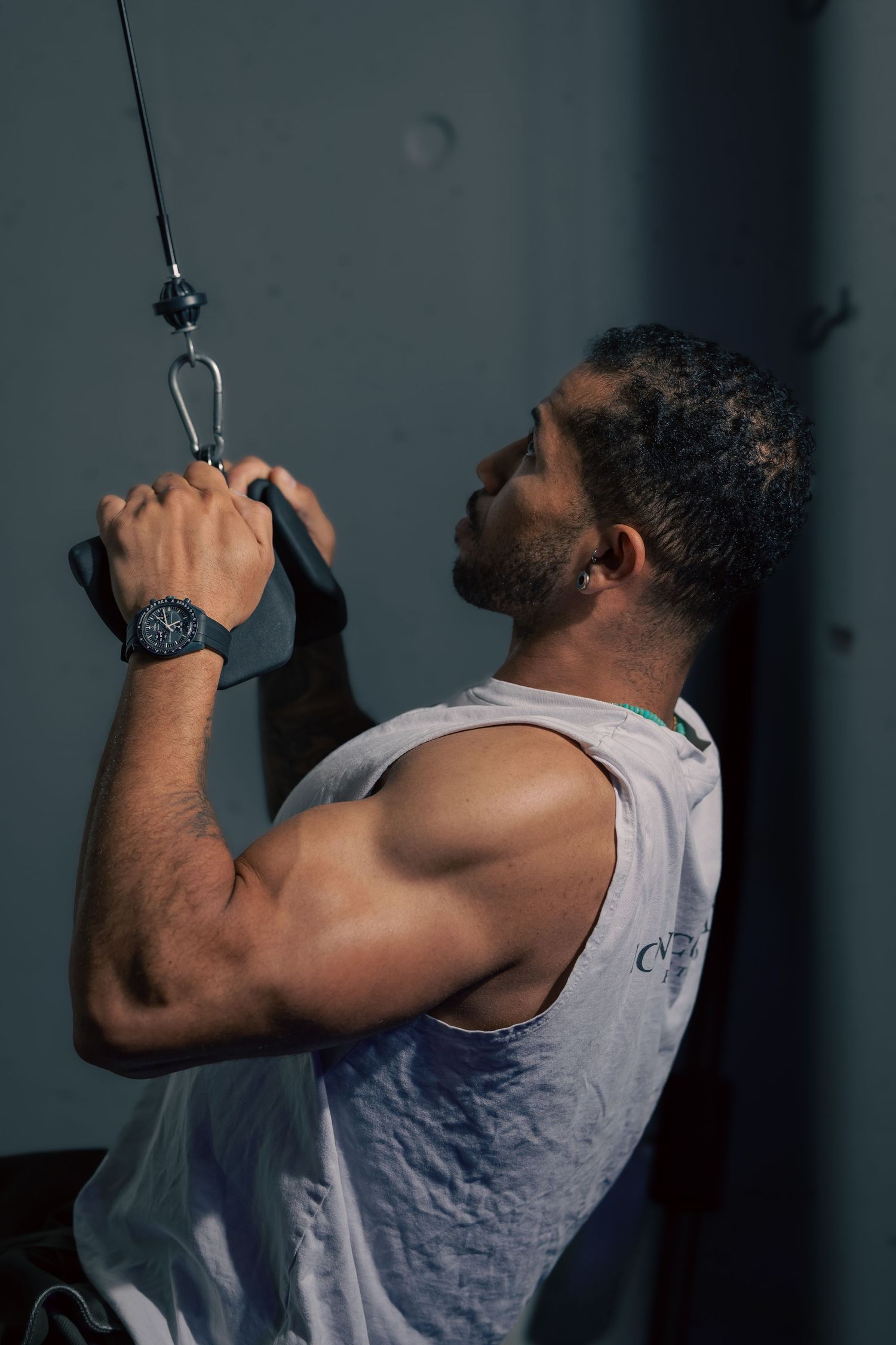Muscular man in white tank top performing cable pulldown exercise at gym, showcasing strong arms and biceps.