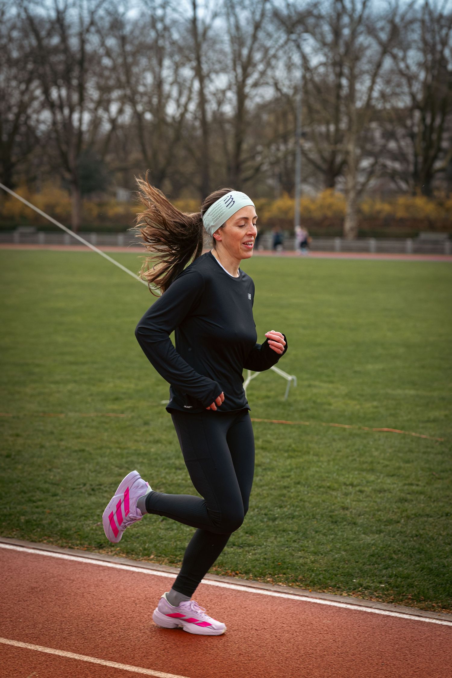 Runner in black athletic wear and headband training on an outdoor track with hair flowing in motion.
